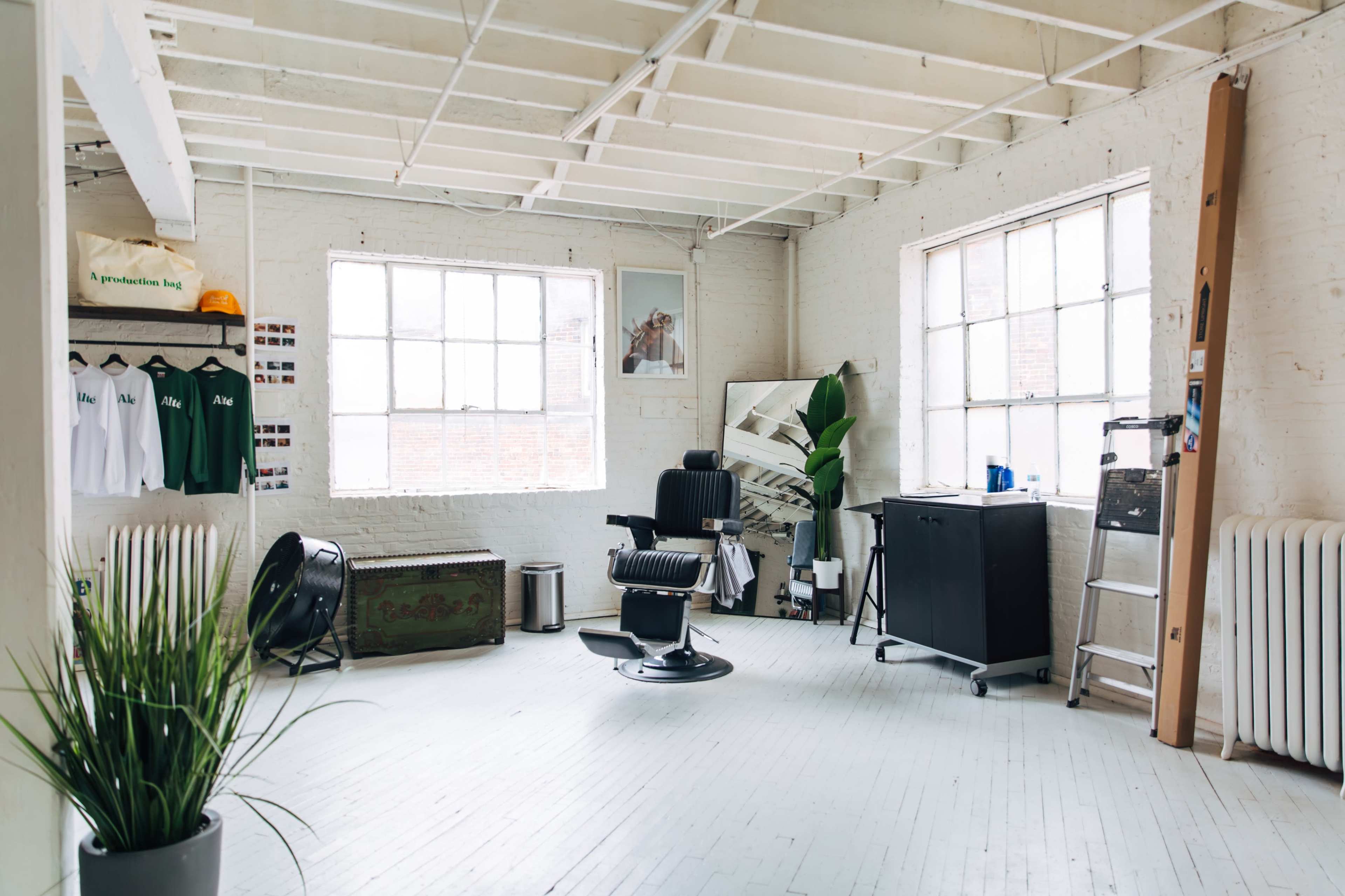 A spacious, well-lit room featuring a barber chair, a potted plant, and various furniture items against exposed brick walls.