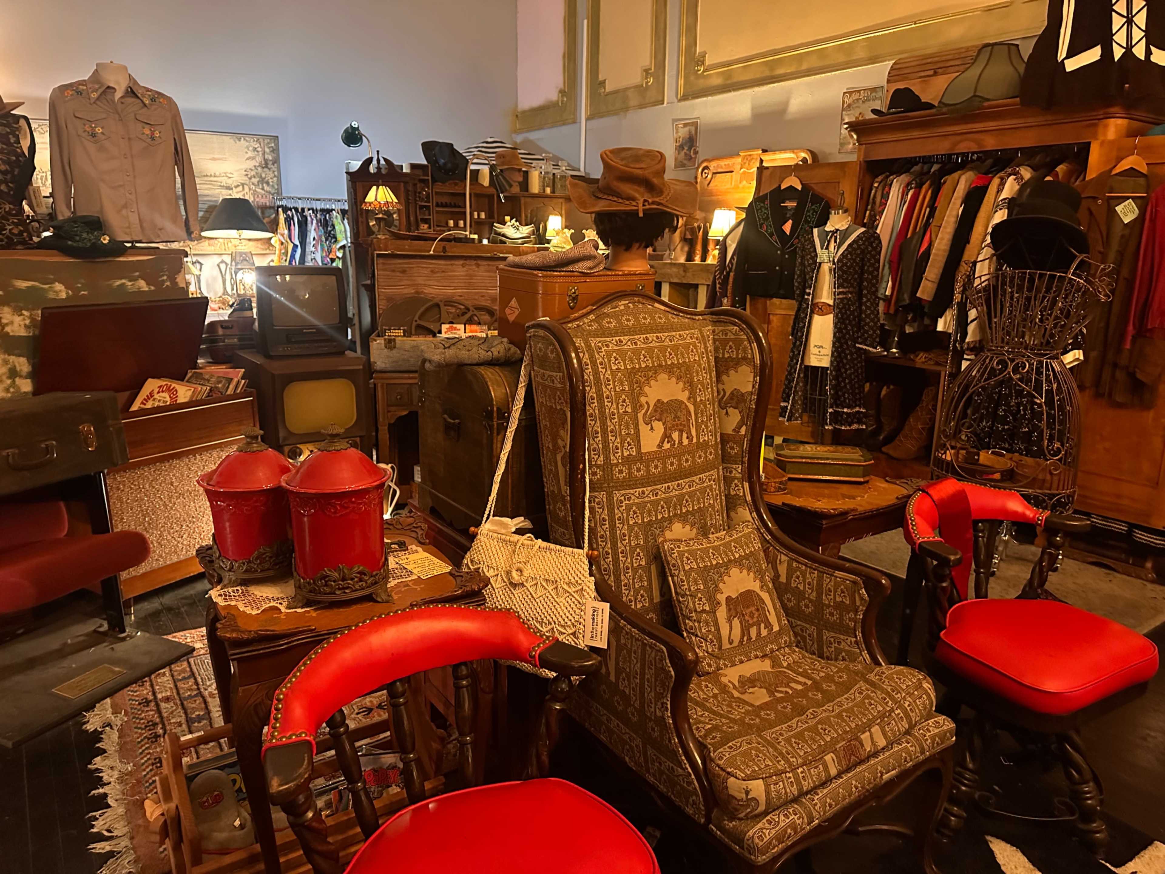 The image shows a vintage shop filled with various antique items, including furniture, clothing, and decorative pieces.