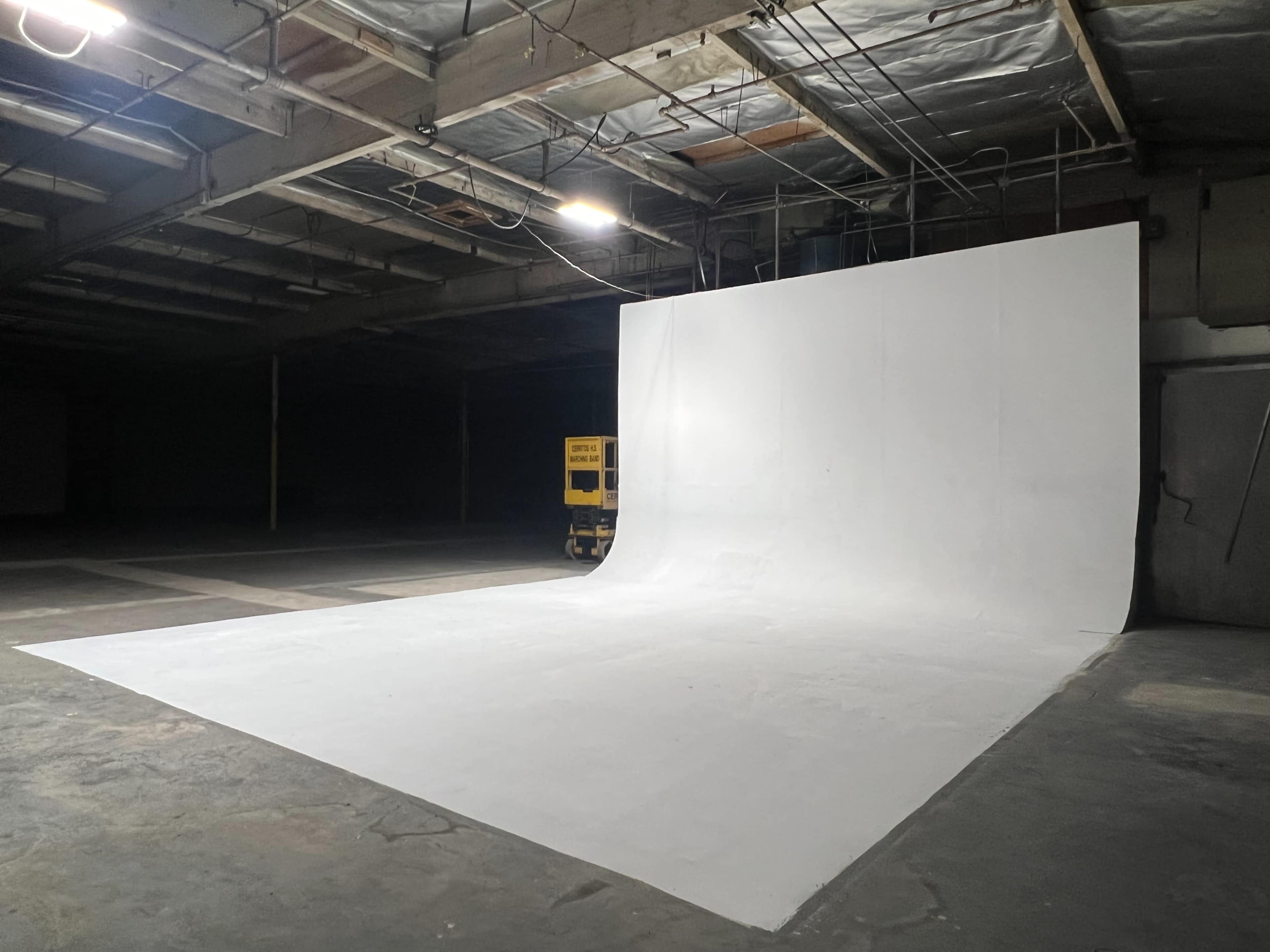 A large, empty studio space with a smooth white backdrop and concrete floor, illuminated by overhead lights.
