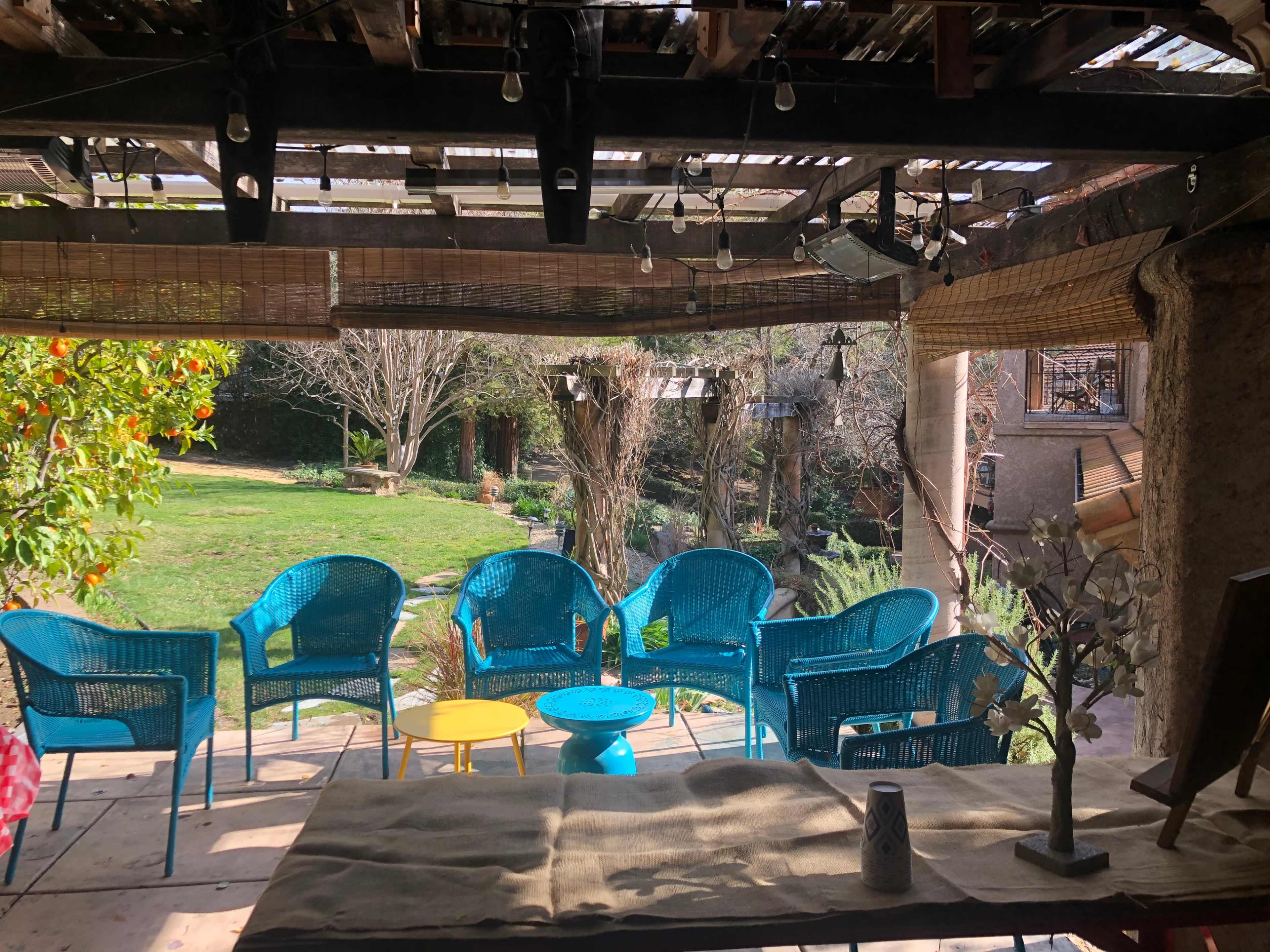 A cozy outdoor seating area with turquoise chairs and a small round yellow table, surrounded by greenery and trees.