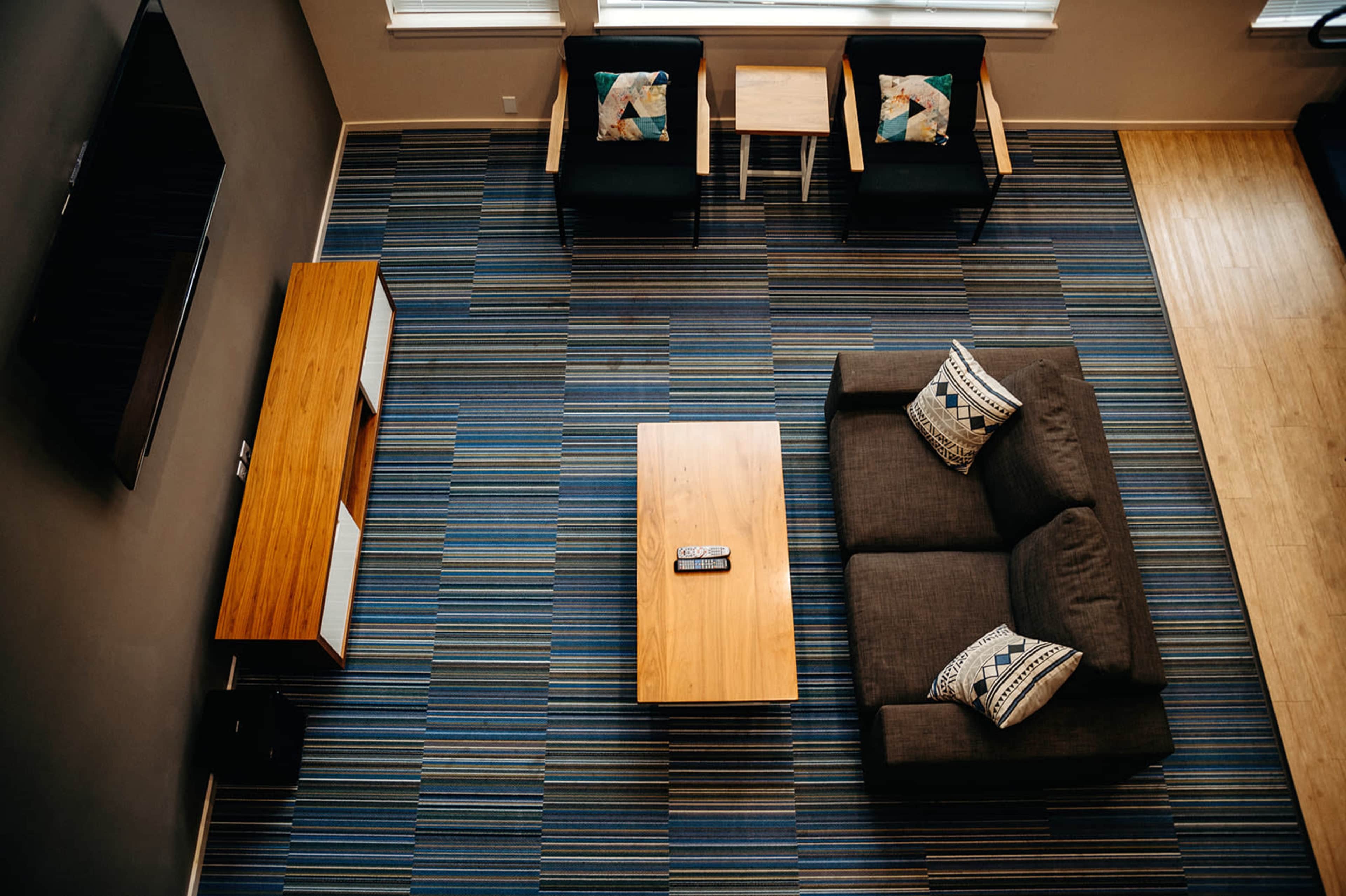 A modern living room with a sectional sofa, a wooden coffee table, two armchairs, and a rug featuring striped patterns.