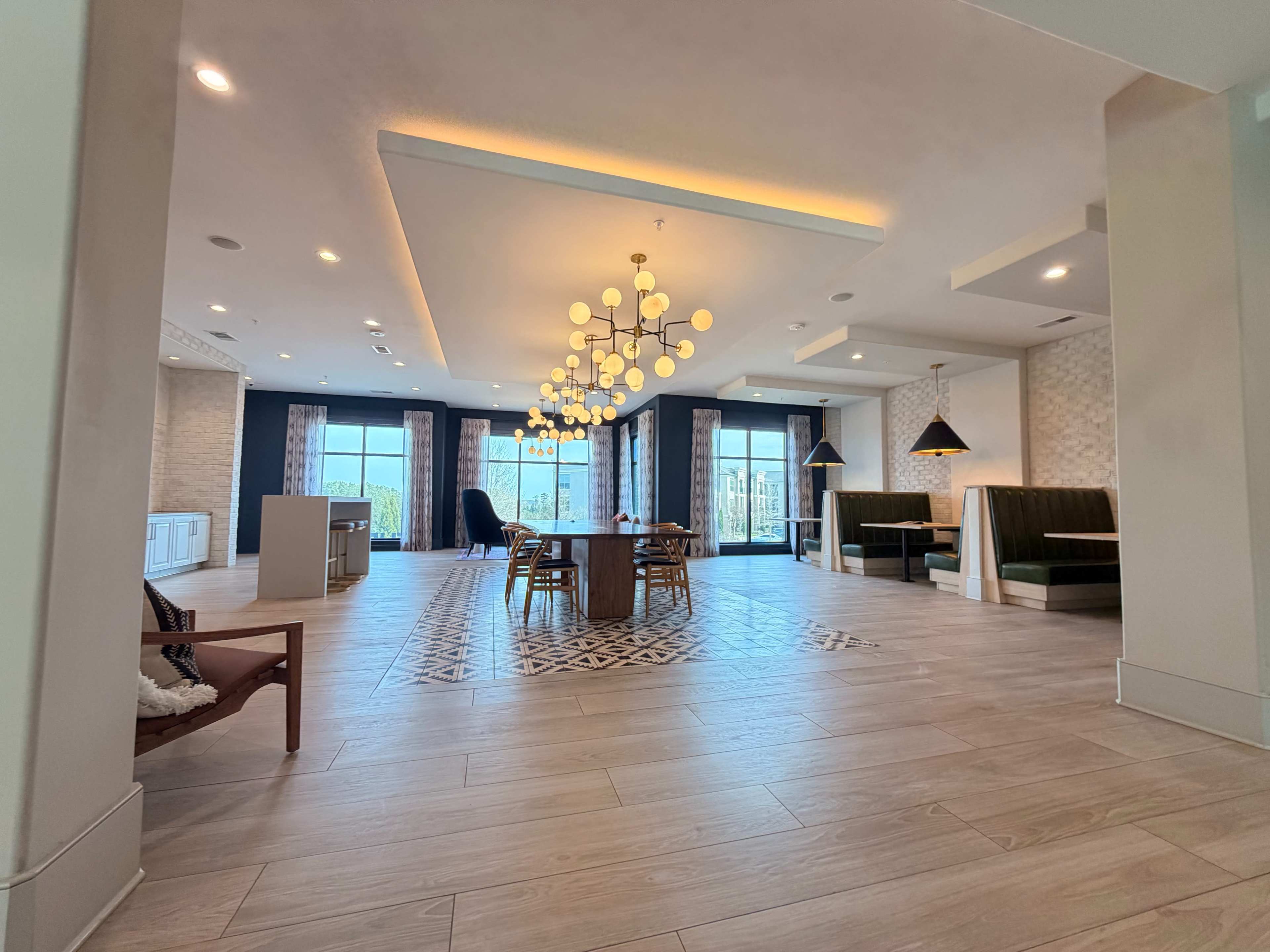 The image depicts a spacious, modern interior with a dining area, stylish lighting fixtures, and large windows that provide natural light.