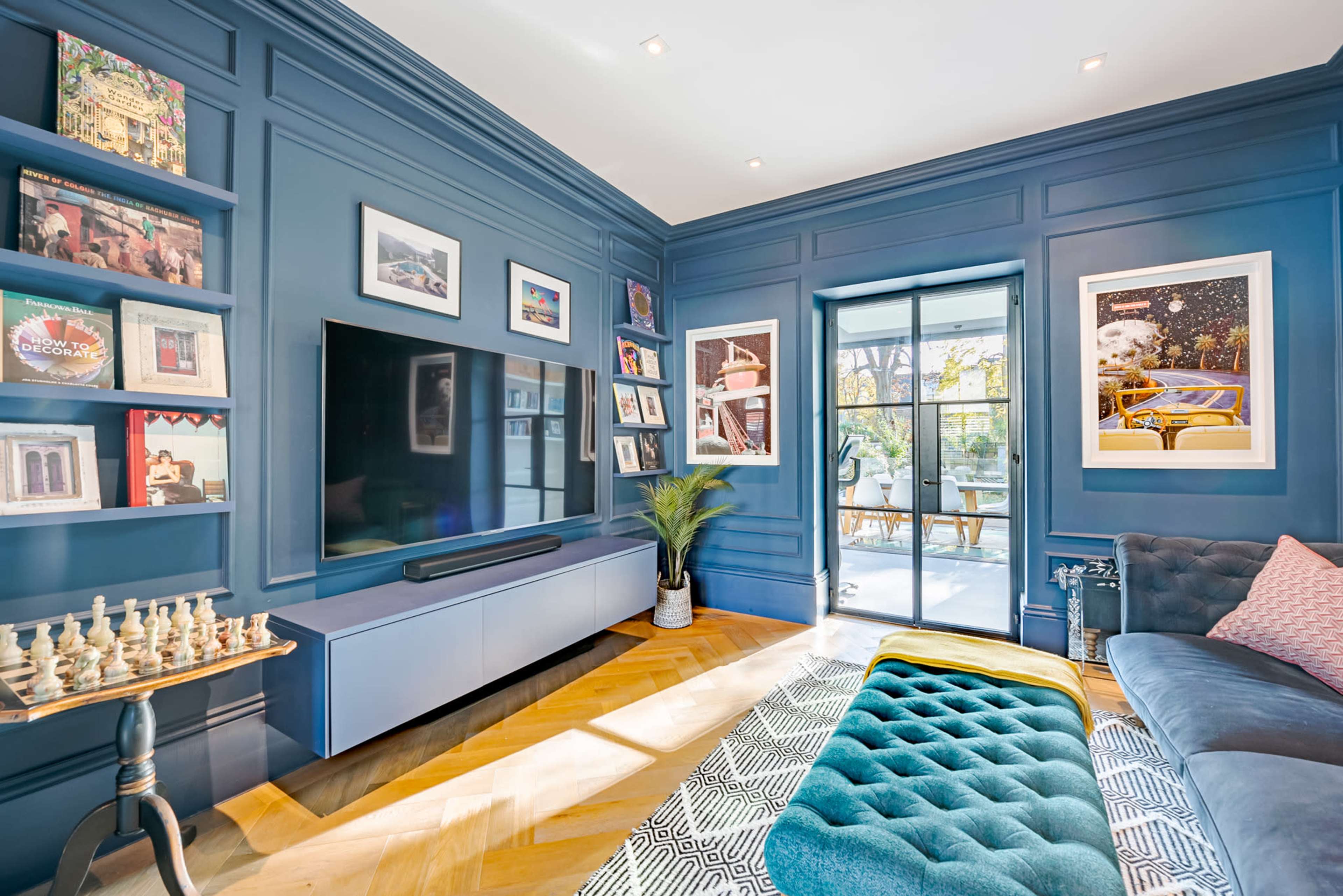 The image features a living room with blue paneled walls, a large television mounted on a media console, and a sliding glass door leading to a patio.