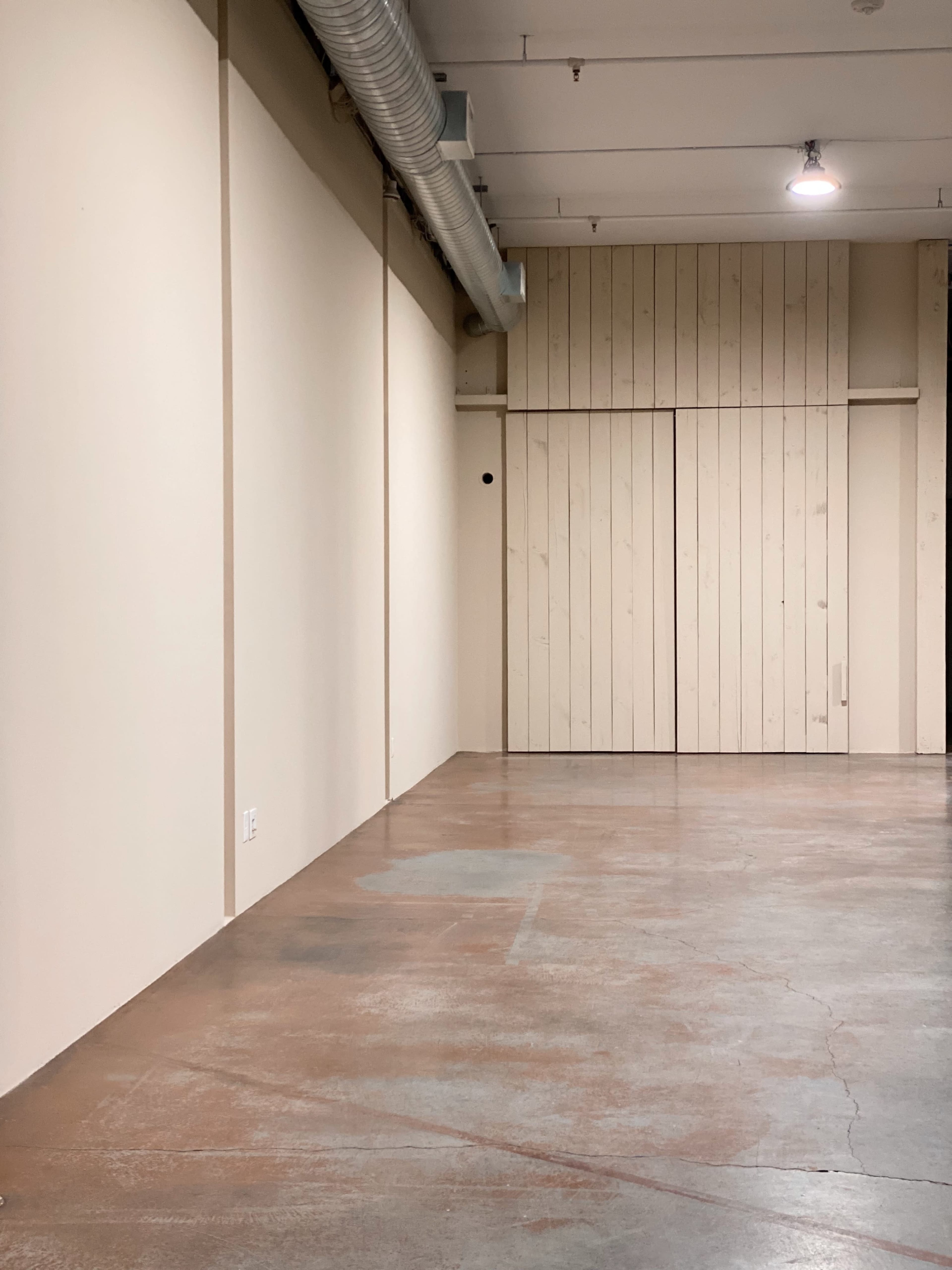 A spacious indoor area with bare walls, a wooden panel door, and a polished concrete floor.