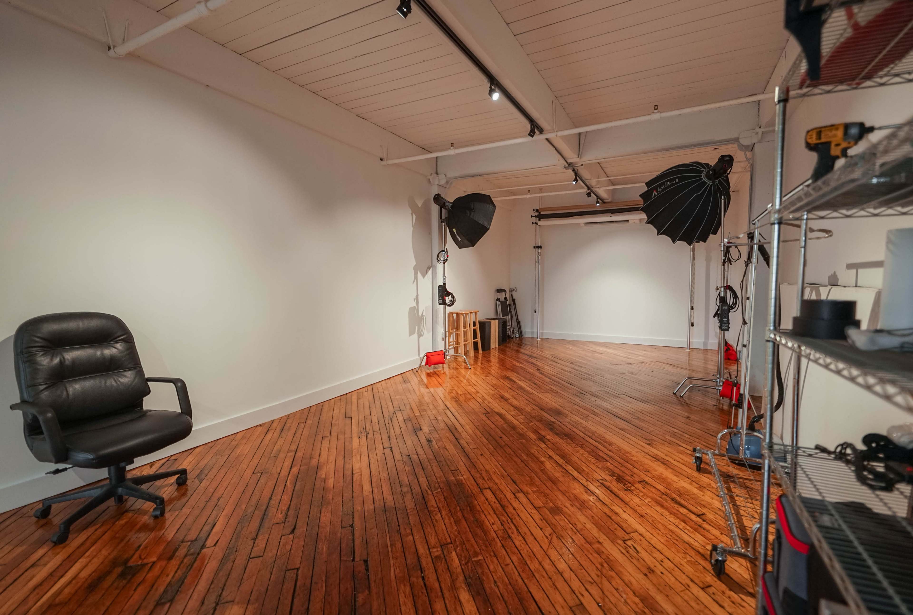 An empty studio space with wooden flooring, two large softbox lights, and a black office chair.