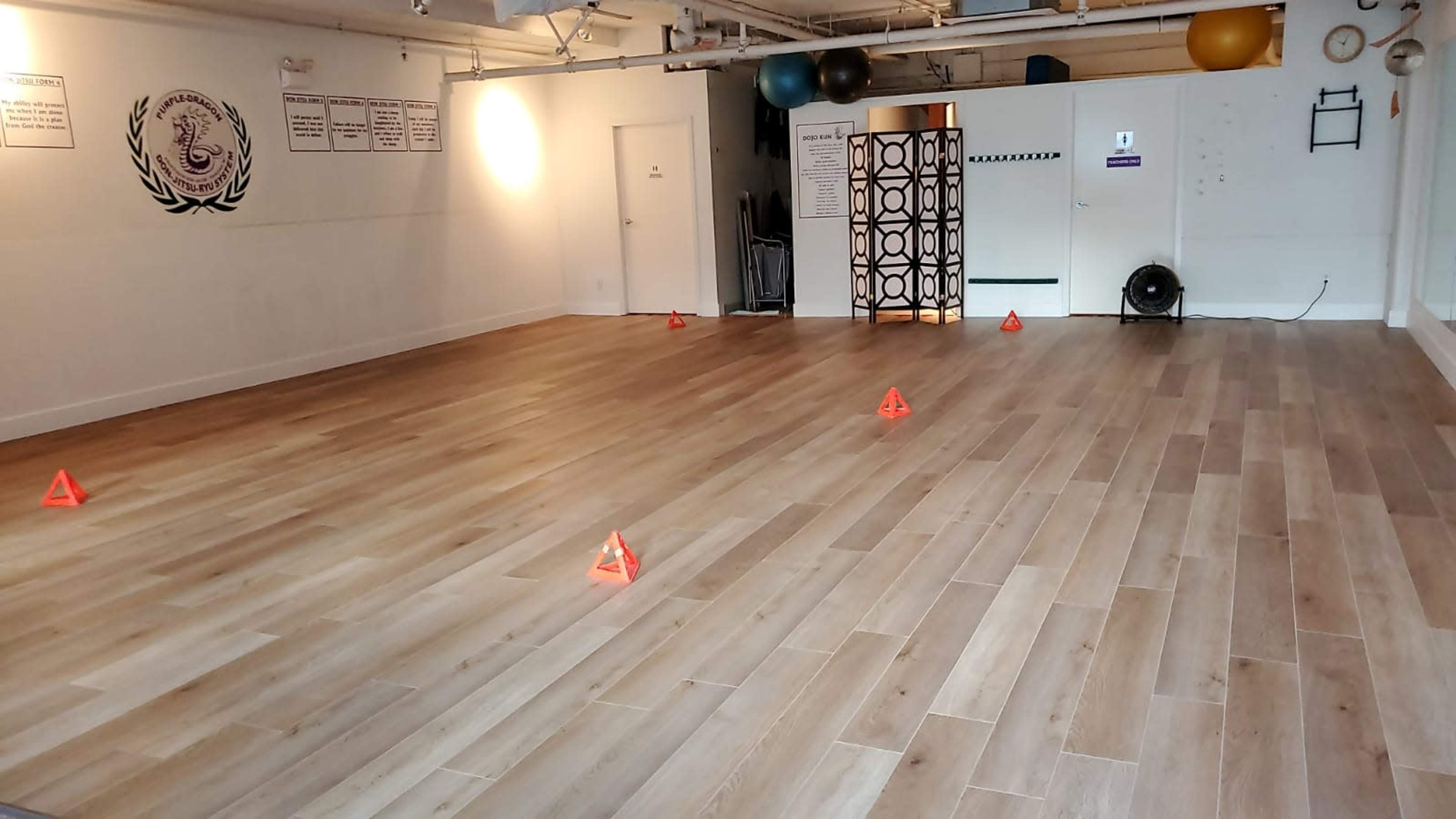 An empty fitness studio features wooden flooring with several red traffic cones arranged on the ground.