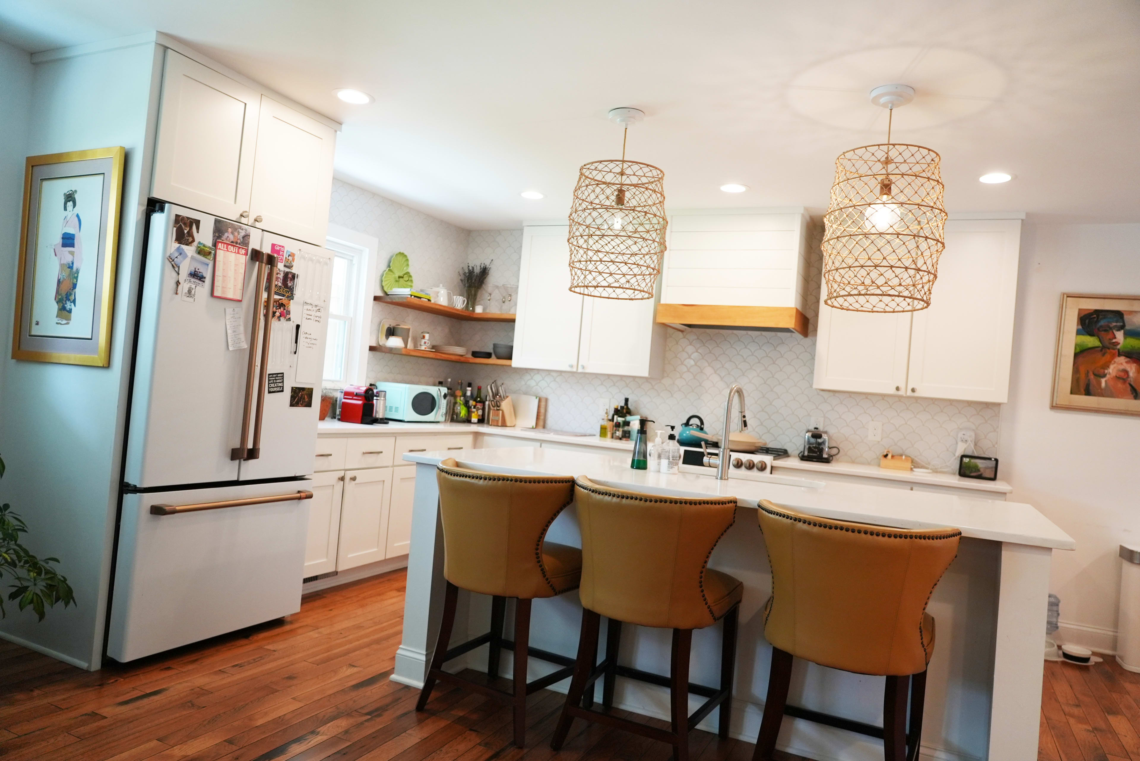 A modern kitchen features a central island with three orange bar stools, white cabinetry, and two hanging light fixtures.