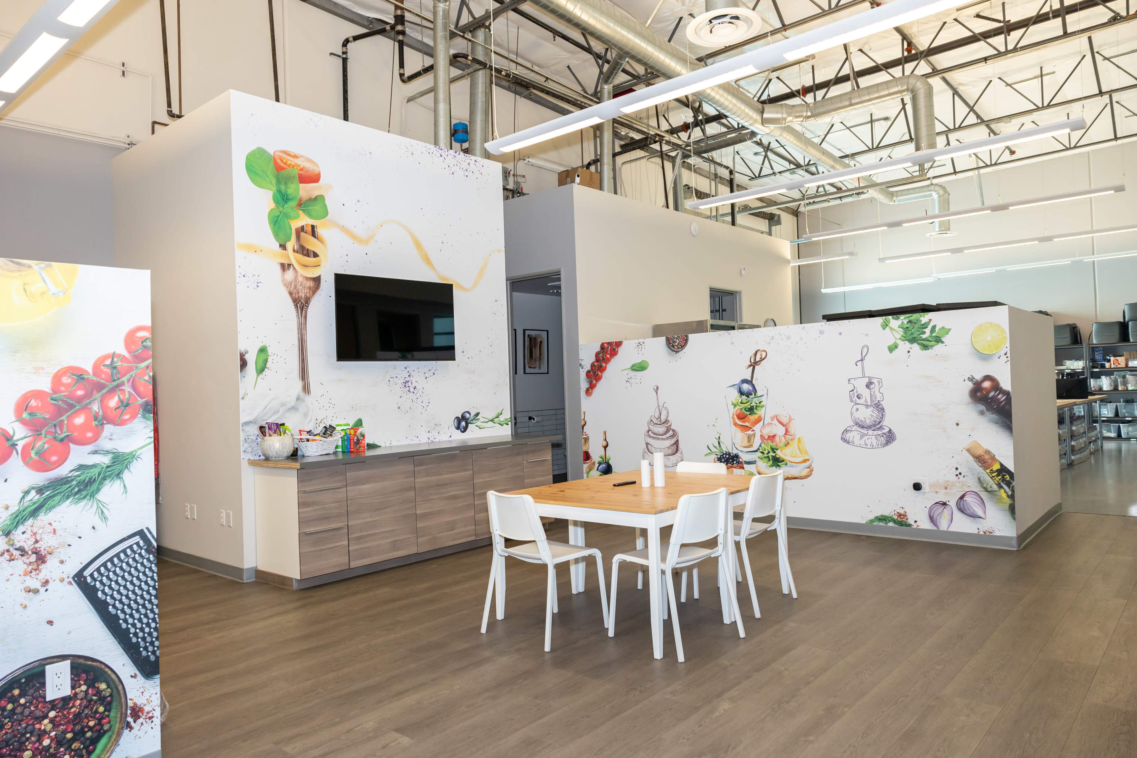 A modern kitchen area with a wooden dining table and walls decorated with colorful food illustrations.