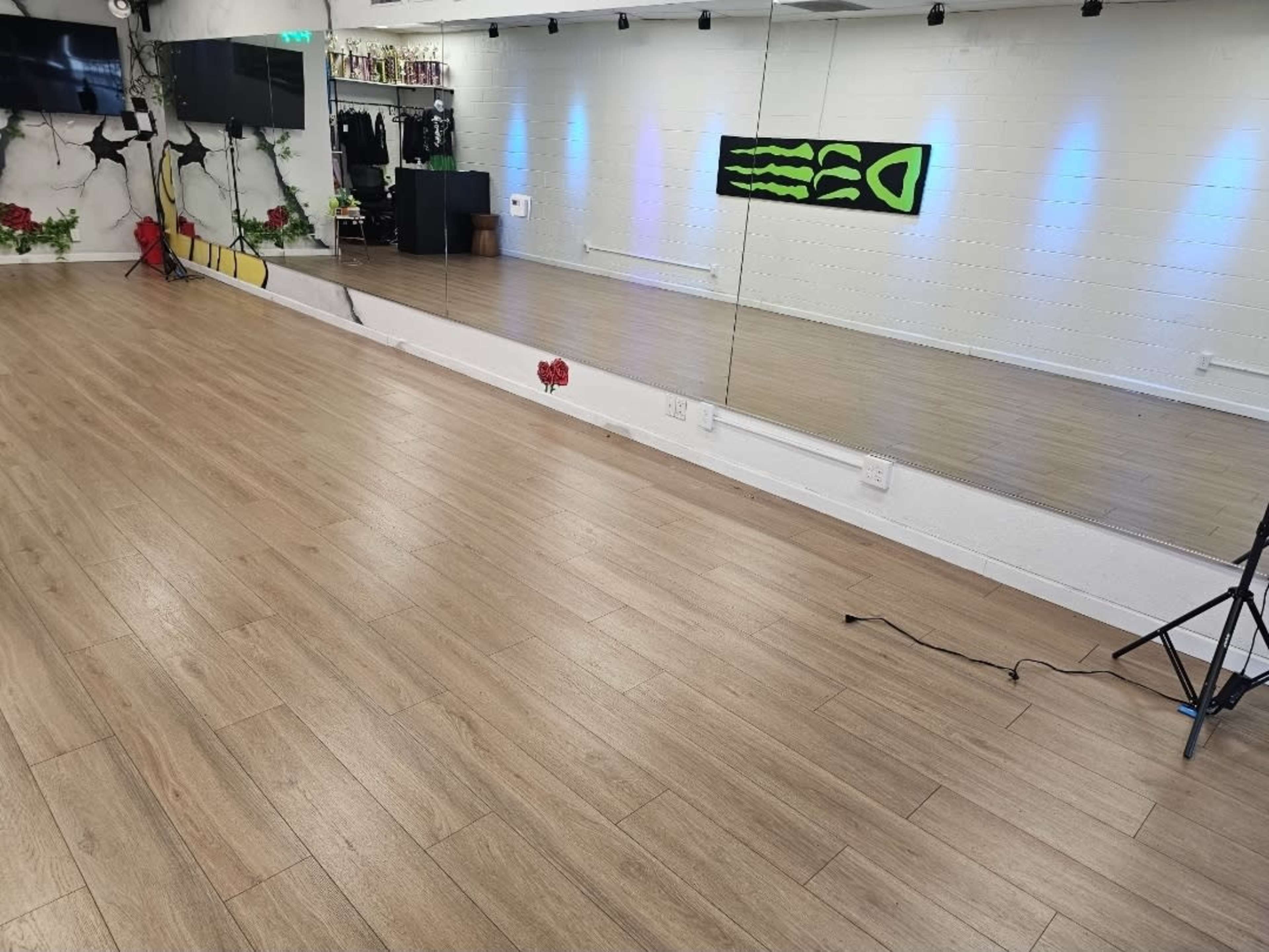 The image shows a spacious dance studio with wooden flooring, a large mirror on one wall, and LED lighting displaying a design.