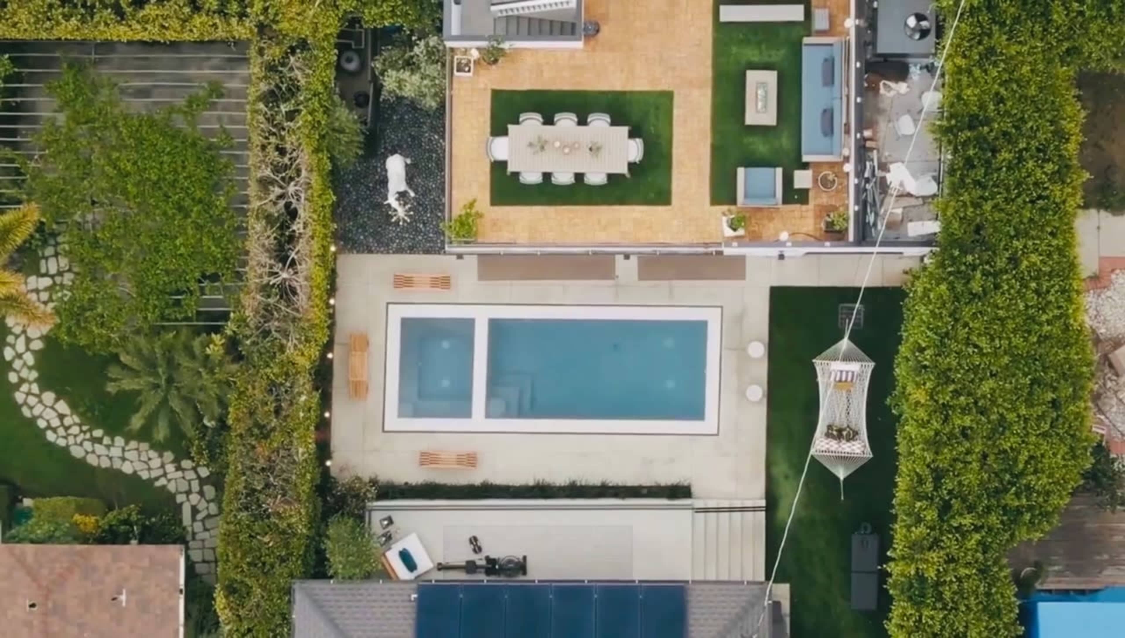 An aerial view of a backyard featuring a rectangular swimming pool, outdoor dining area, and landscaped greenery.