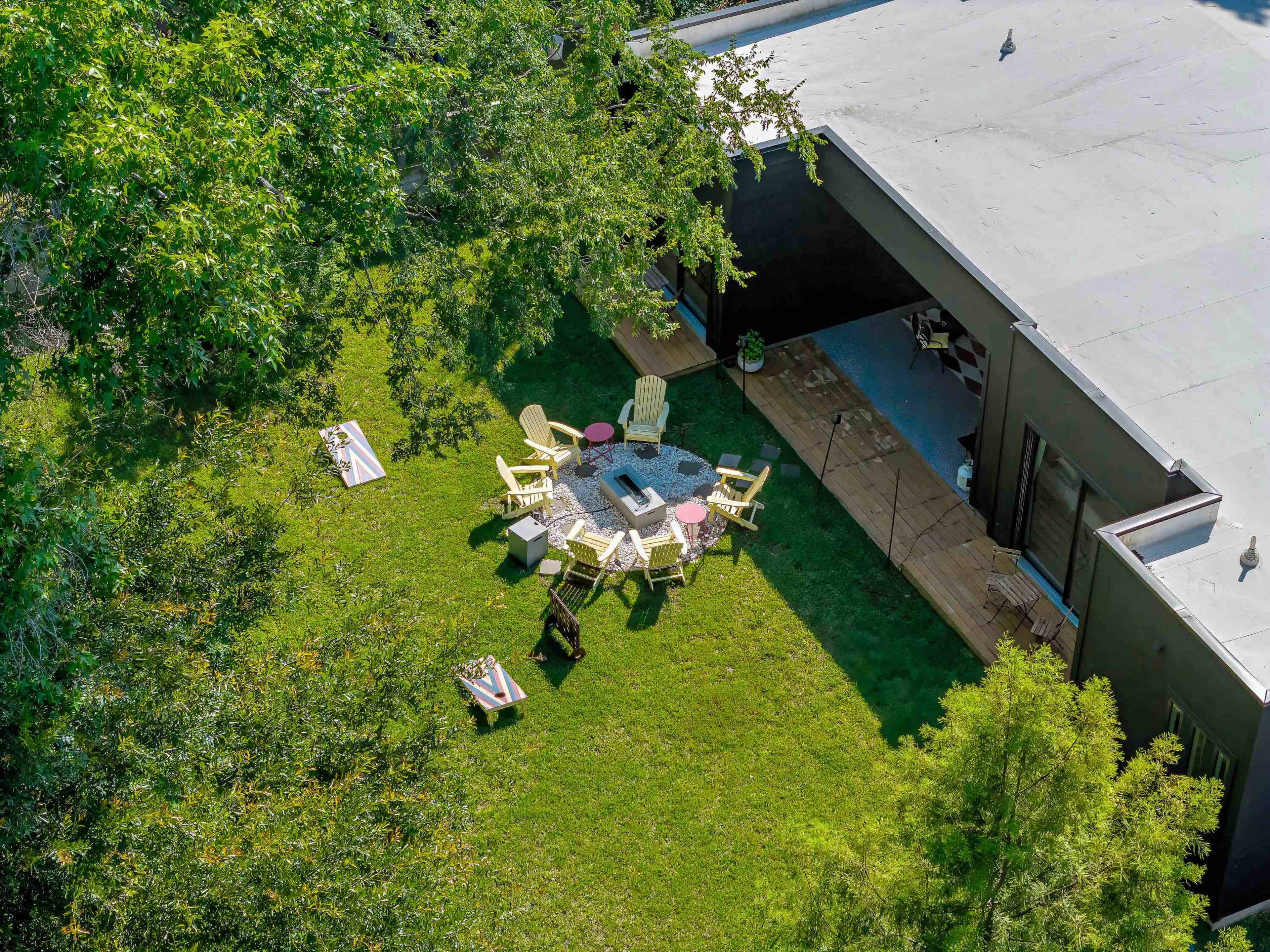 An aerial view shows a circular seating arrangement with several chairs and a fire pit on a grassy area next to a modern building.