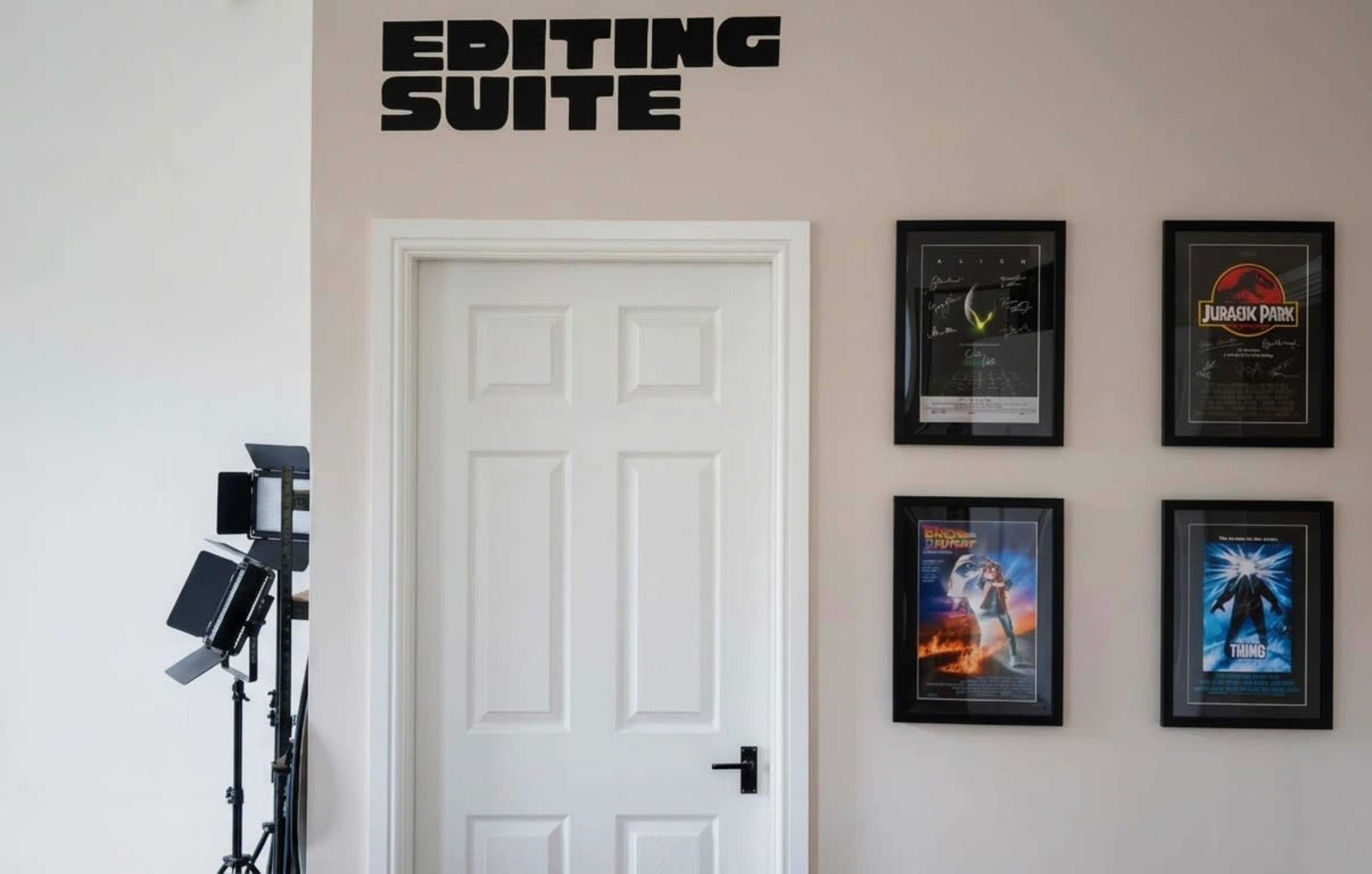 The image shows a white door labeled "Editing Suite" on a wall, surrounded by framed movie posters and studio lights in the background.
