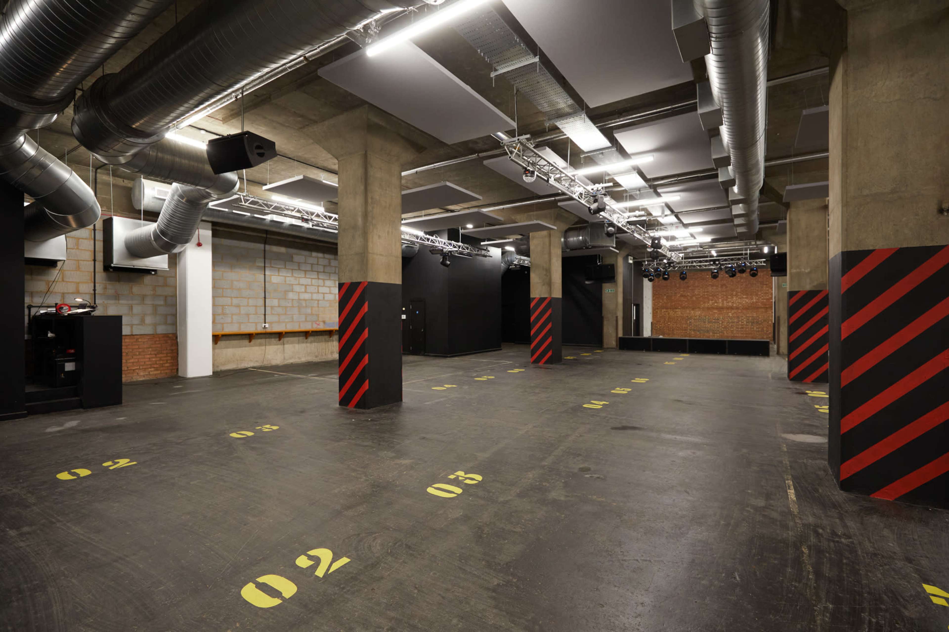 An empty industrial space with exposed concrete walls, black and yellow striped pillars, and overhead lighting fixtures.
