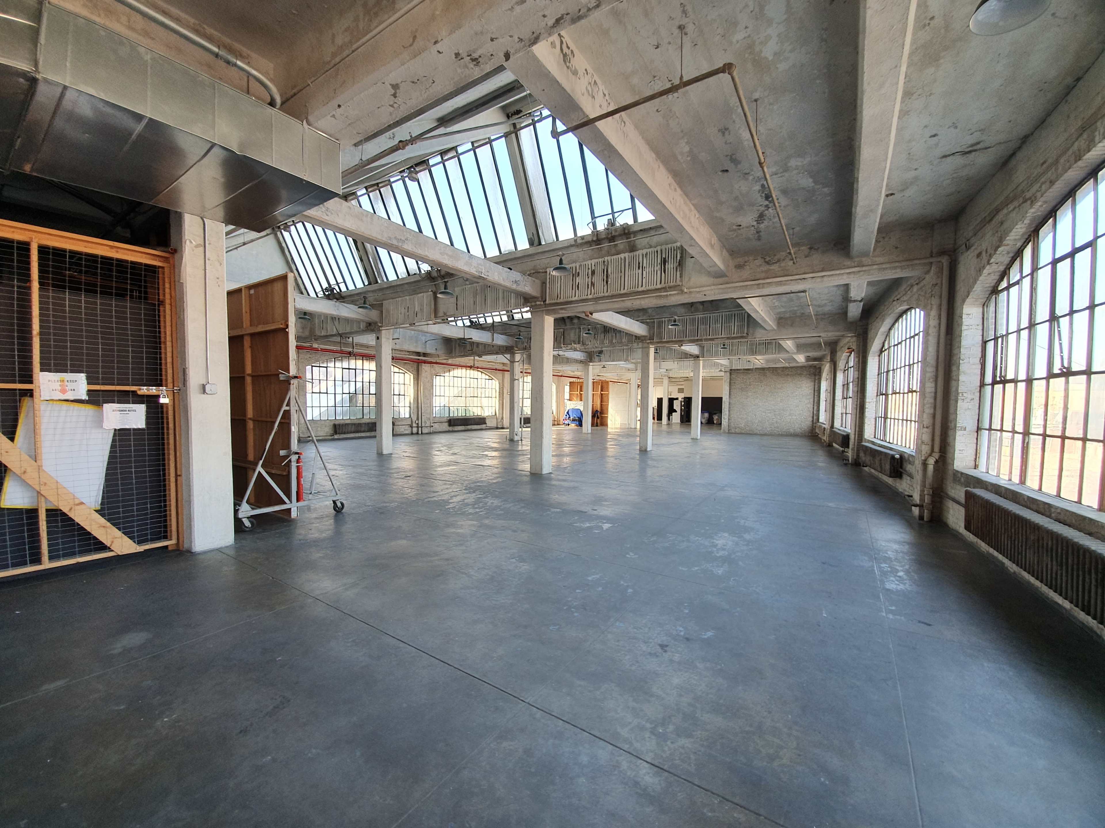 A large, empty industrial space with exposed concrete walls, tall windows, and concrete floors.
