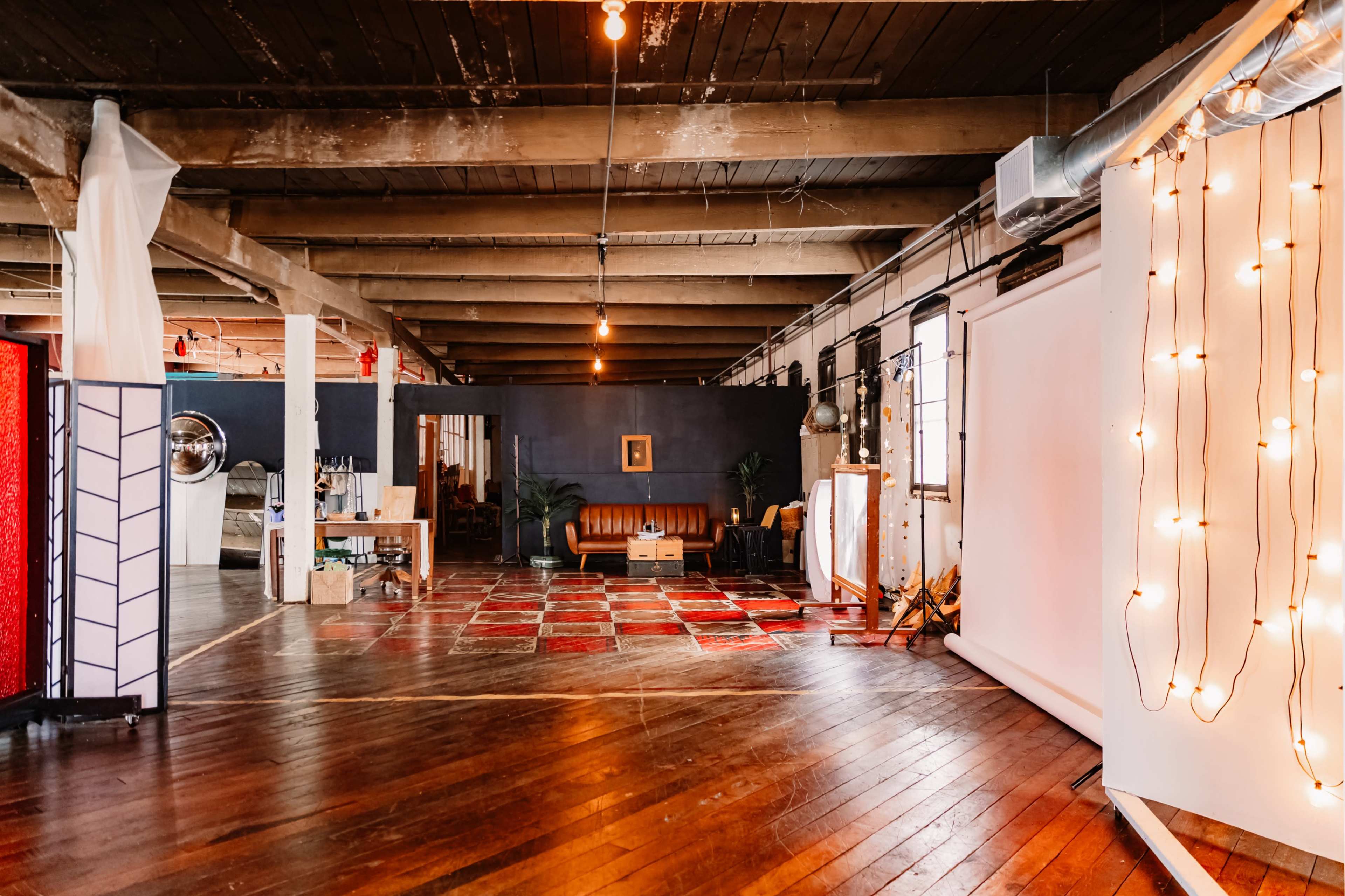 The image shows a spacious, rustic interior with wooden floors, exposed beams, and various seating areas, including a leather sofa, along with creative lighting elements.