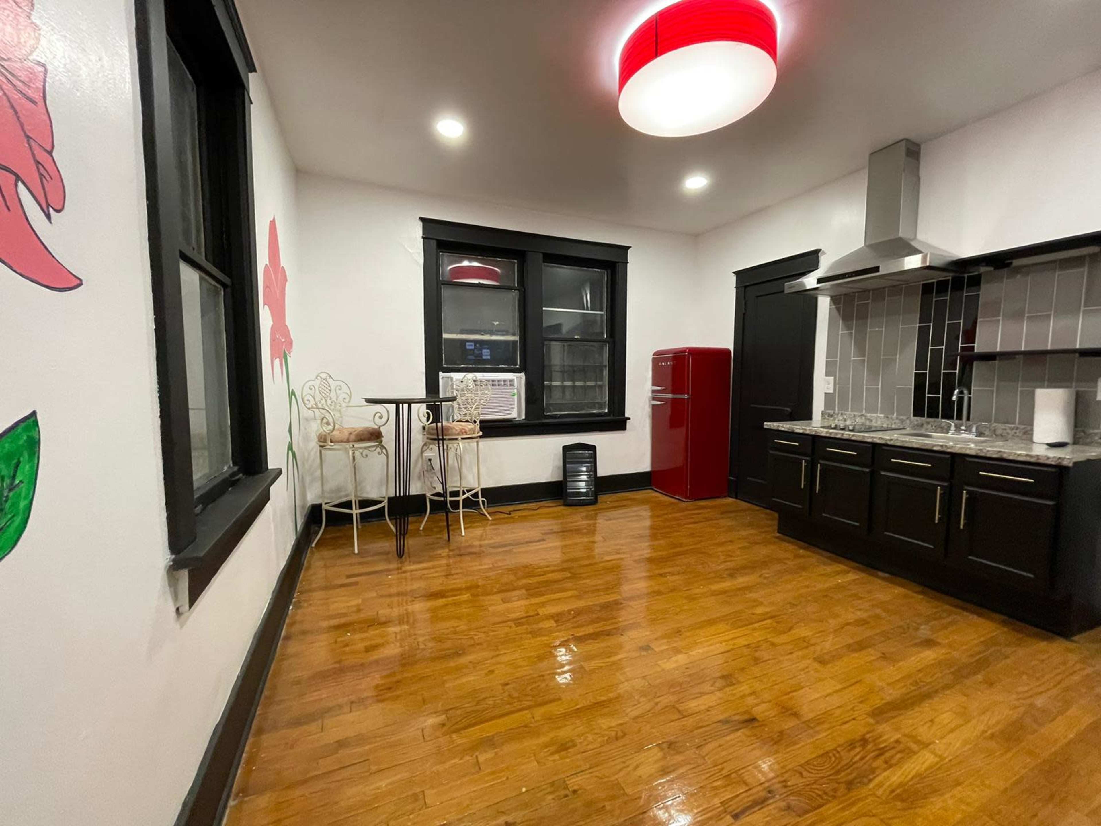 A modern kitchen features dark cabinetry, a red refrigerator, and a small dining area with two chairs against a wall.