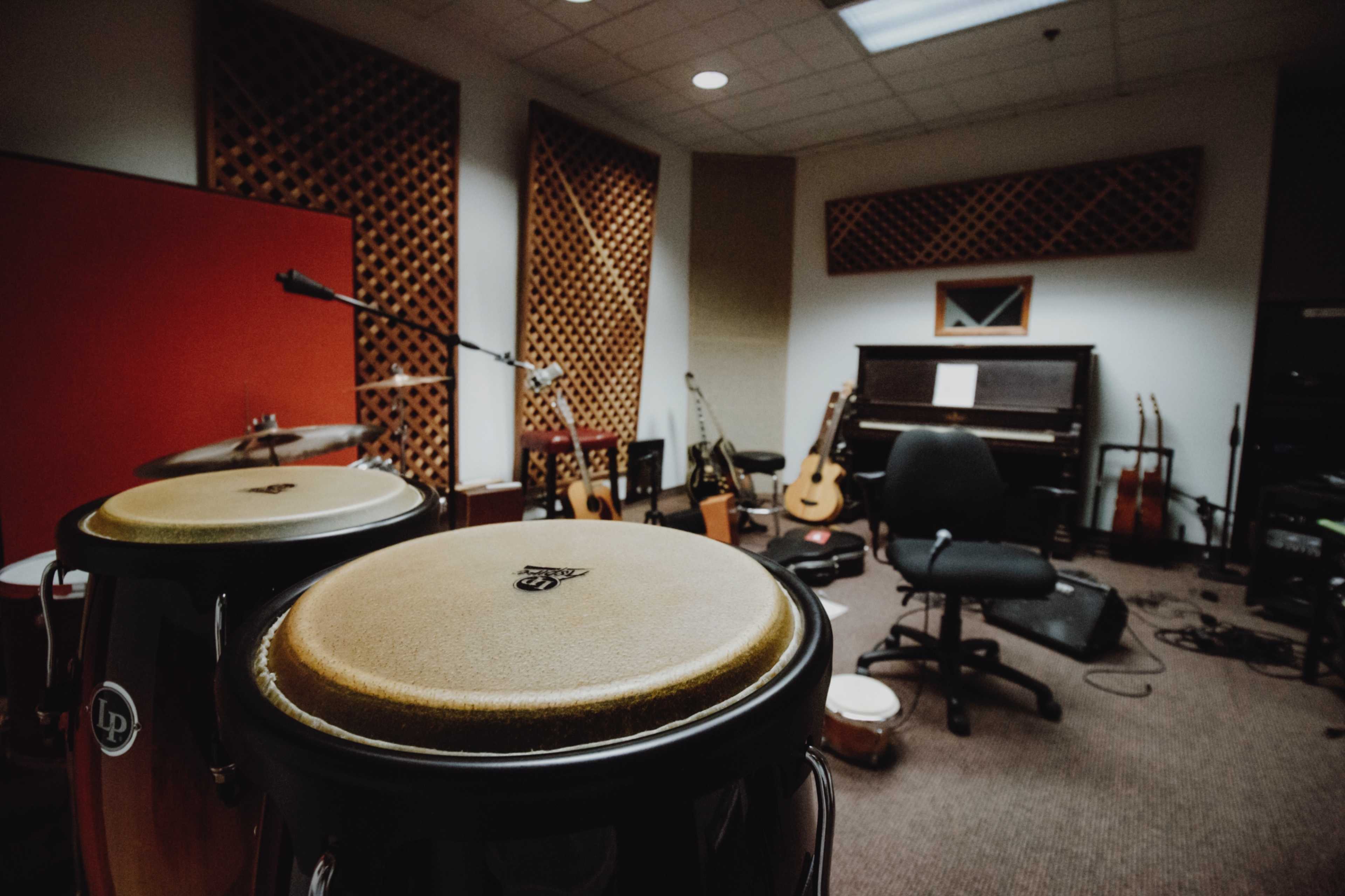 A music studio contains various instruments, including congas, guitars, and a piano, with a chair positioned in the center of the room.