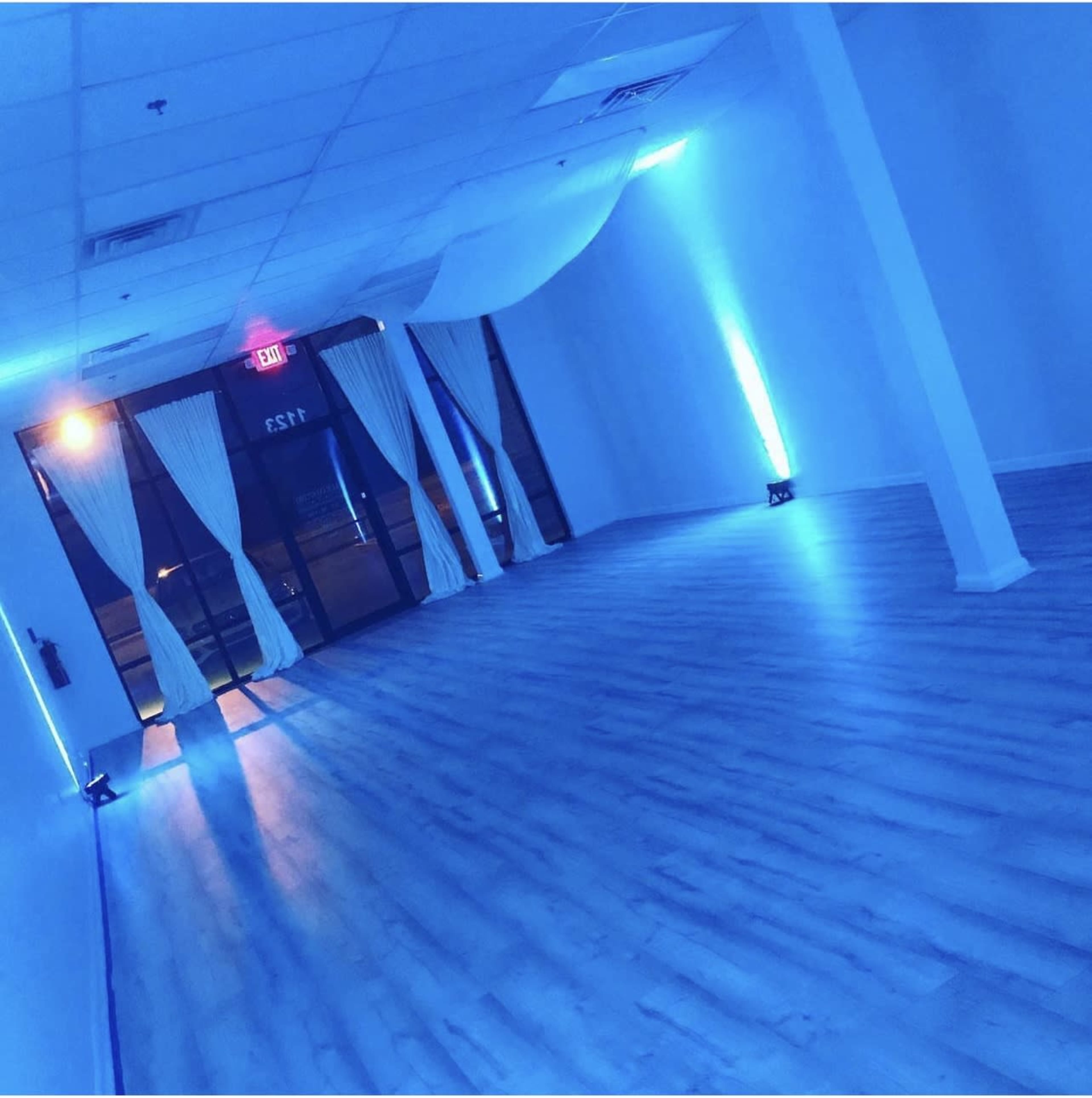 An empty room with blue lighting, white curtains, and a smooth wooden floor.