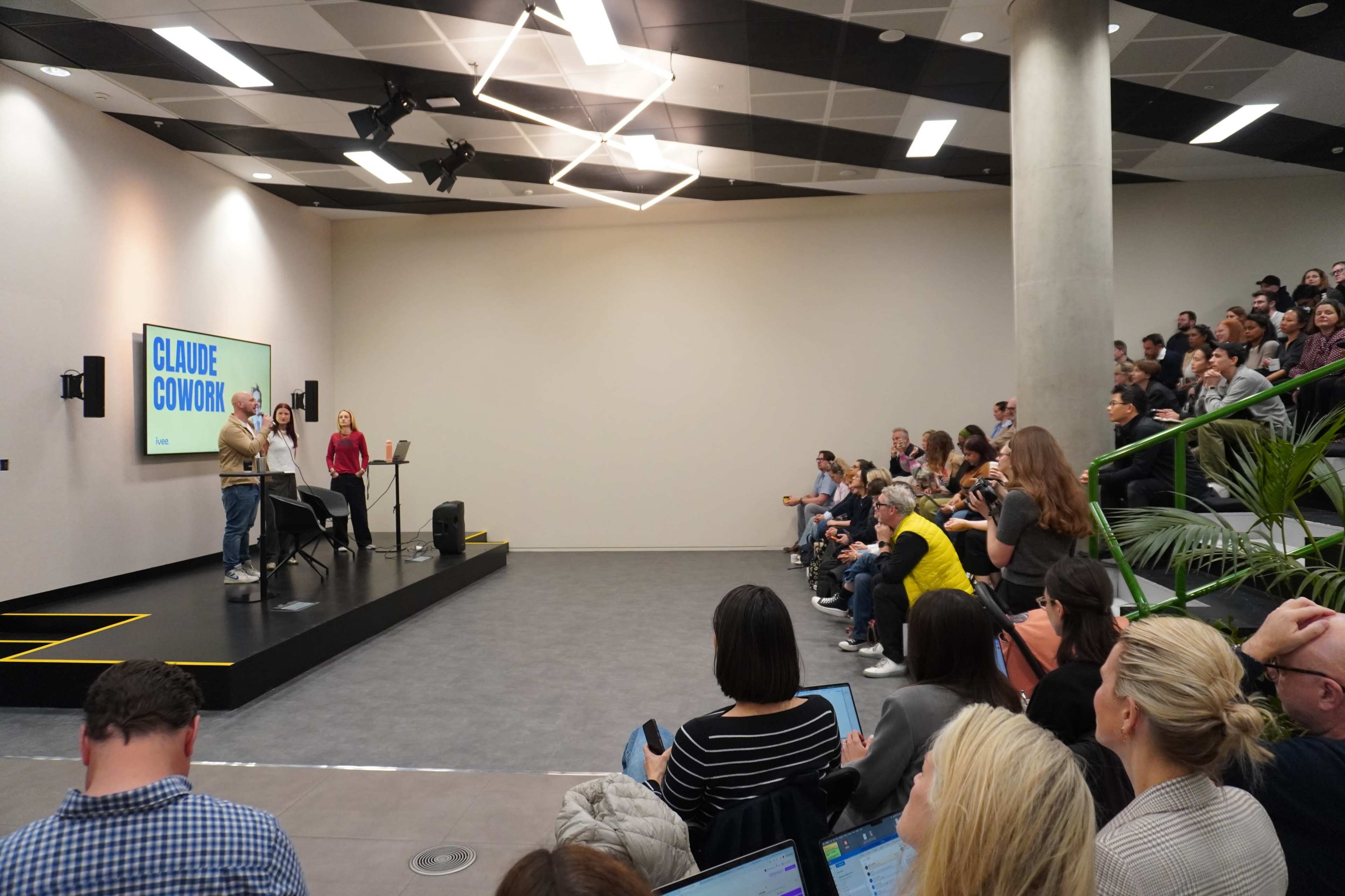 A speaker presents on stage to an audience seated in a modern auditorium.