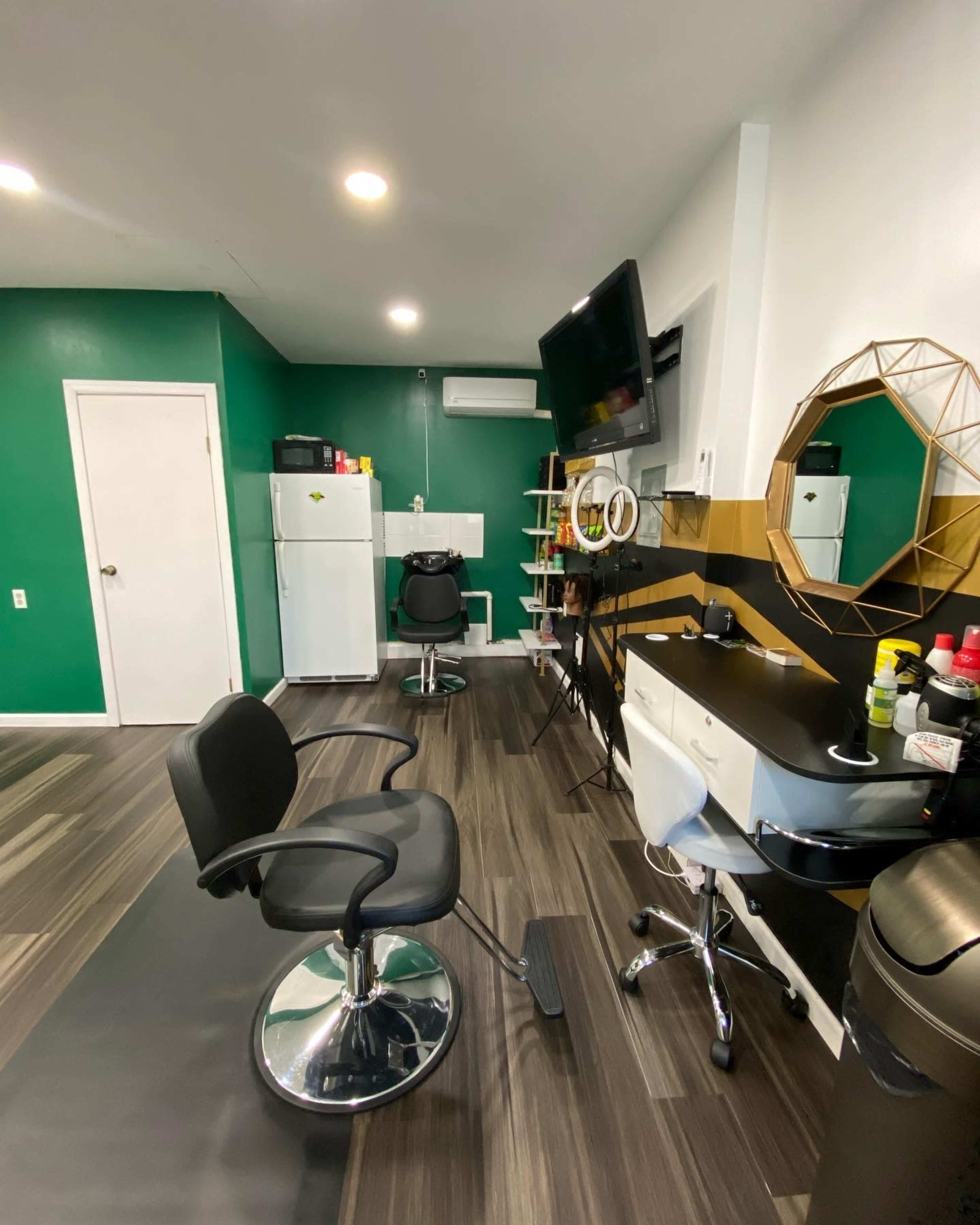 A modern hair salon interior with two styling stations, a refrigerator, and a wall-mounted television, all set against a green and black color scheme.