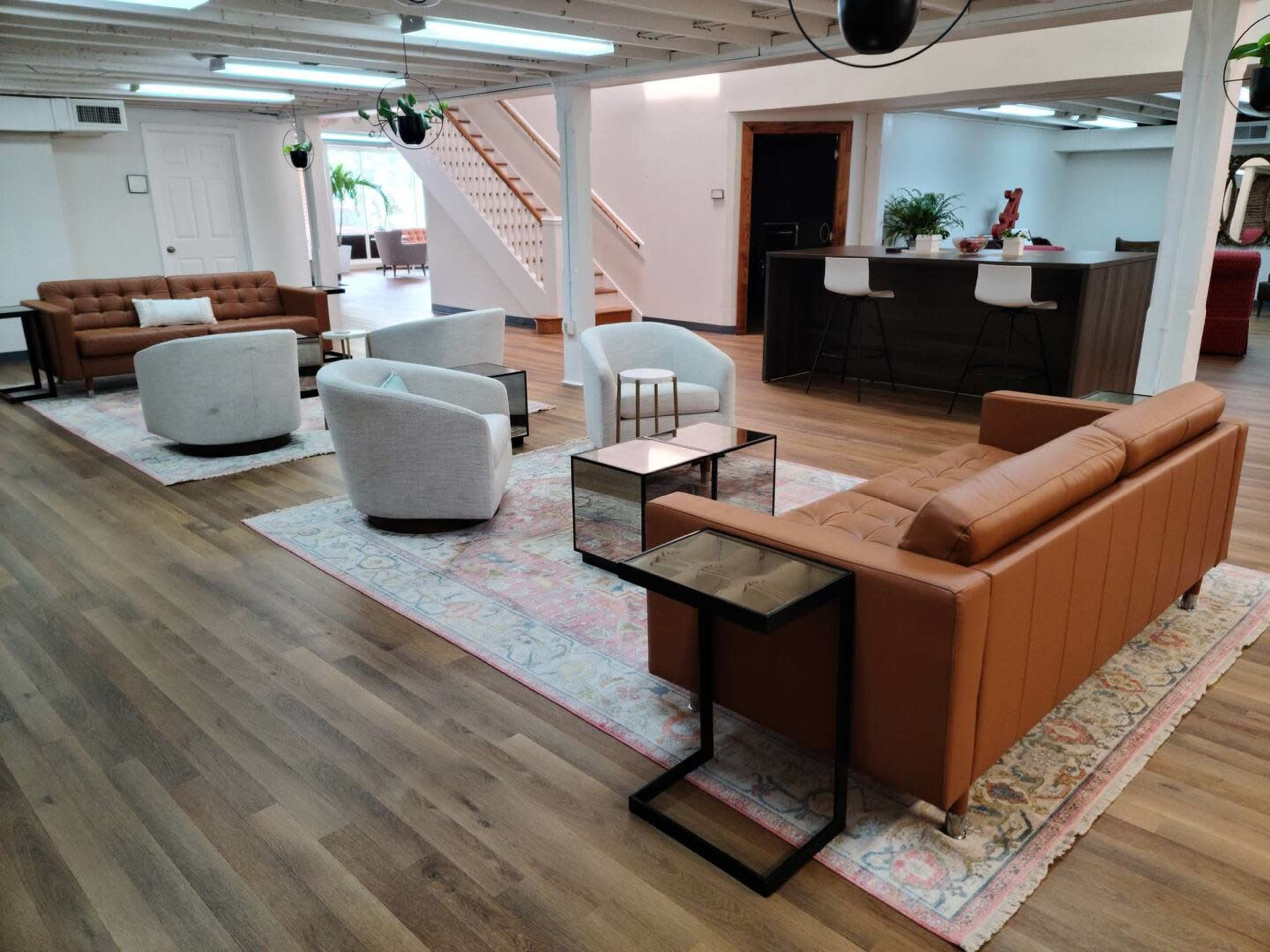 A spacious interior with several modern seating arrangements, including brown leather sofas and circular armchairs, arranged around small black side tables on a decorative rug.