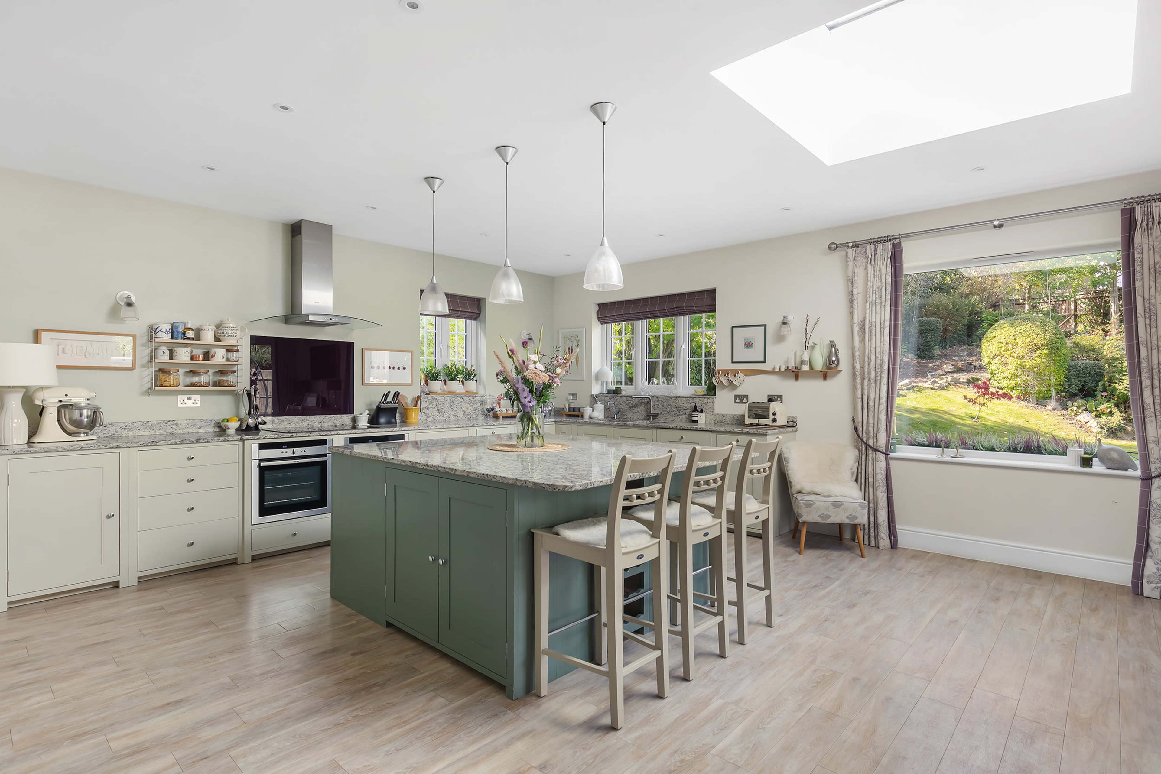 A modern kitchen featuring an island with seating, a stove, and large windows overlooking a garden.