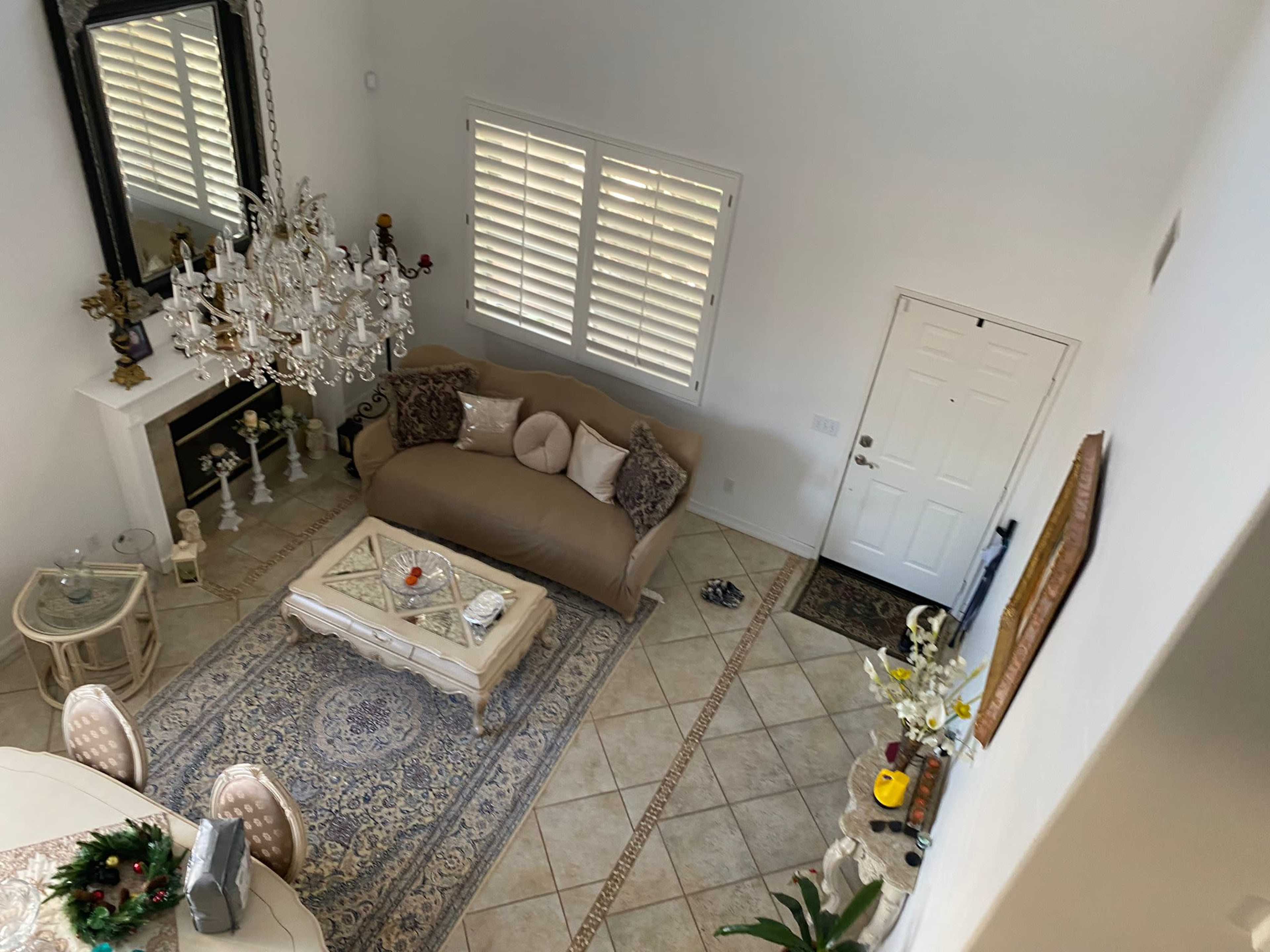 The image shows an aerial view of a living room with a chandelier, a beige sofa, a coffee table, and a door leading outside.