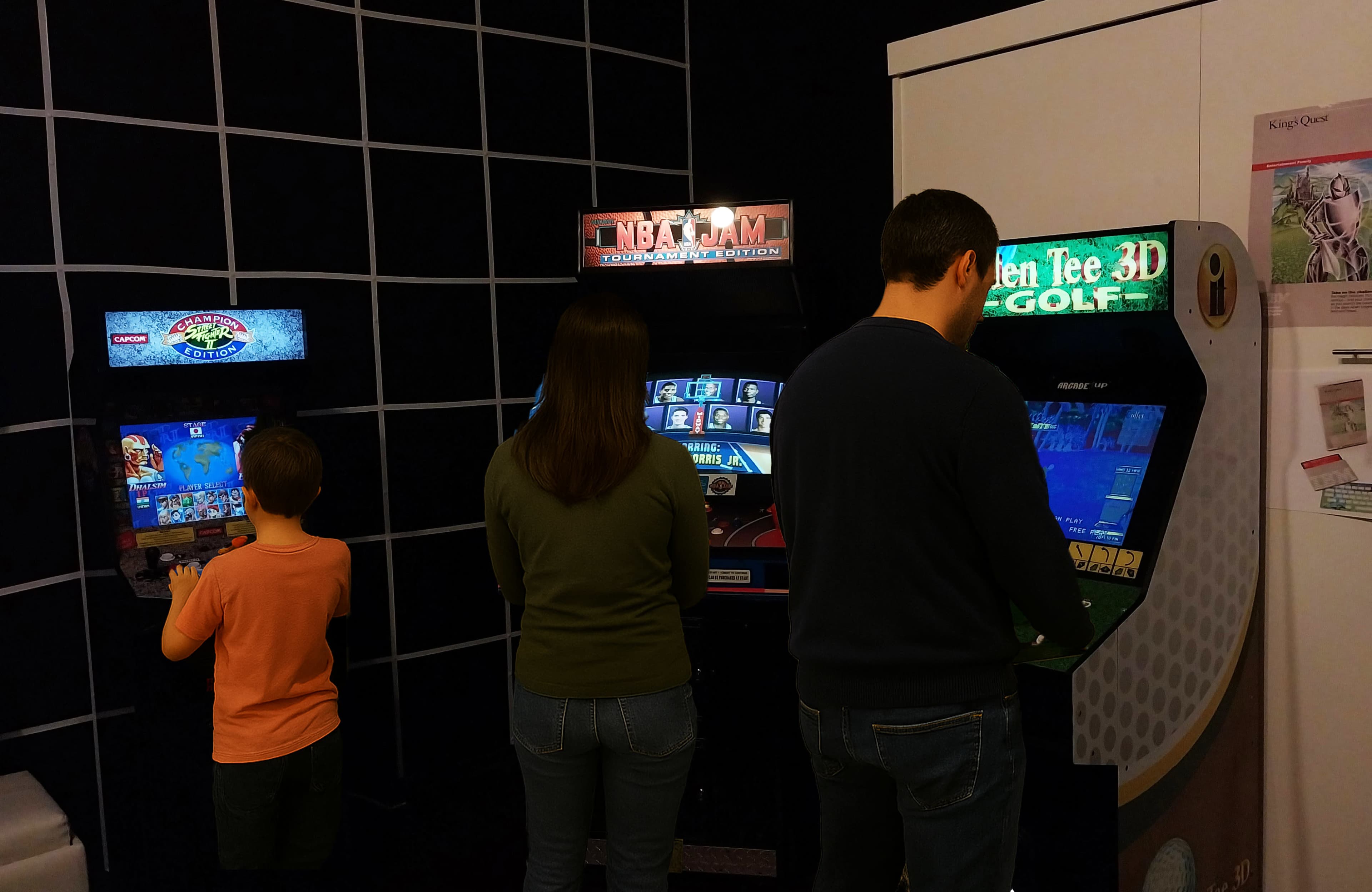 Three people are playing different arcade games at a gaming venue.