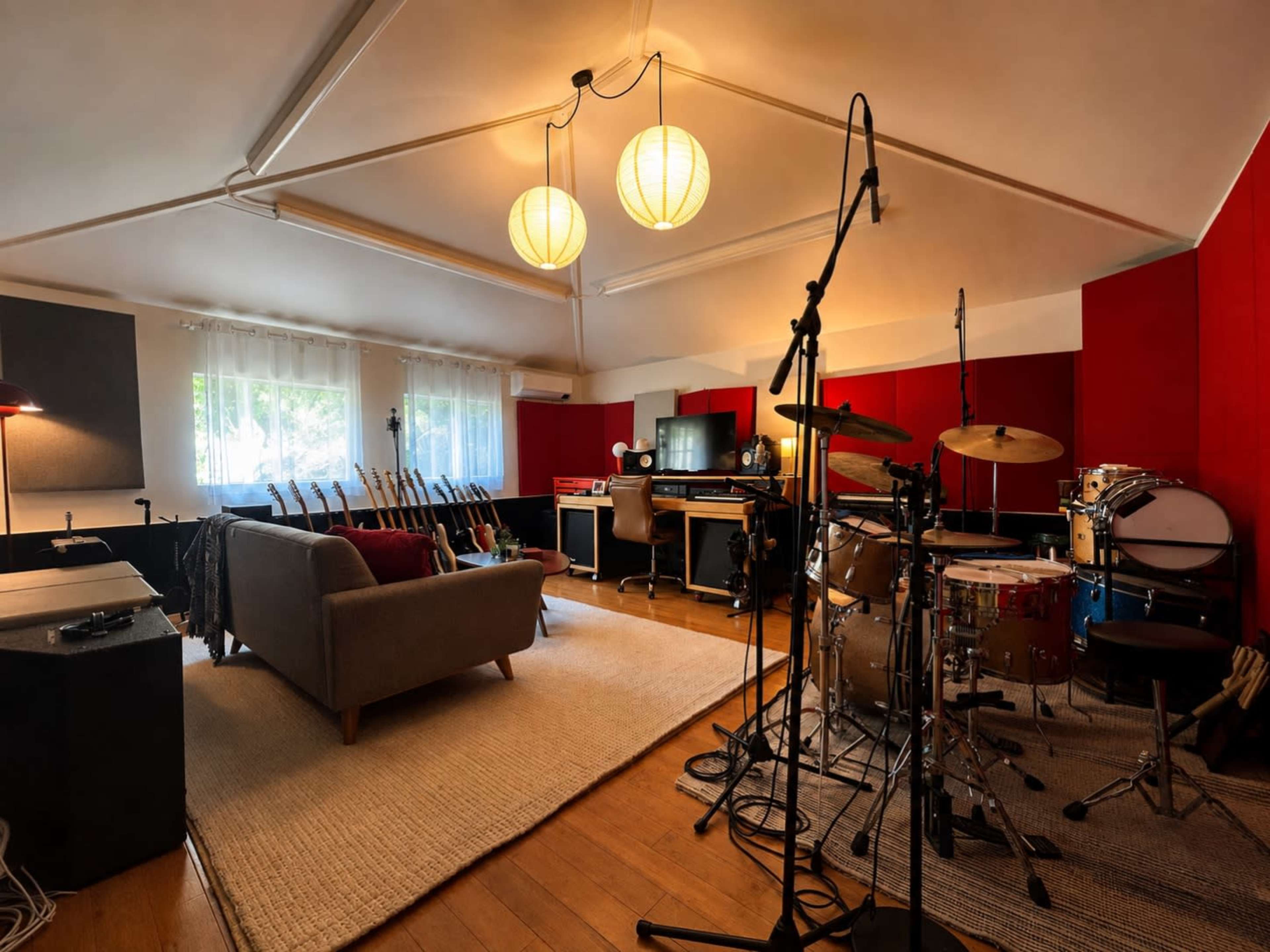 The image shows a well-equipped music studio with various instruments, including a drum set, and a comfortable seating area.