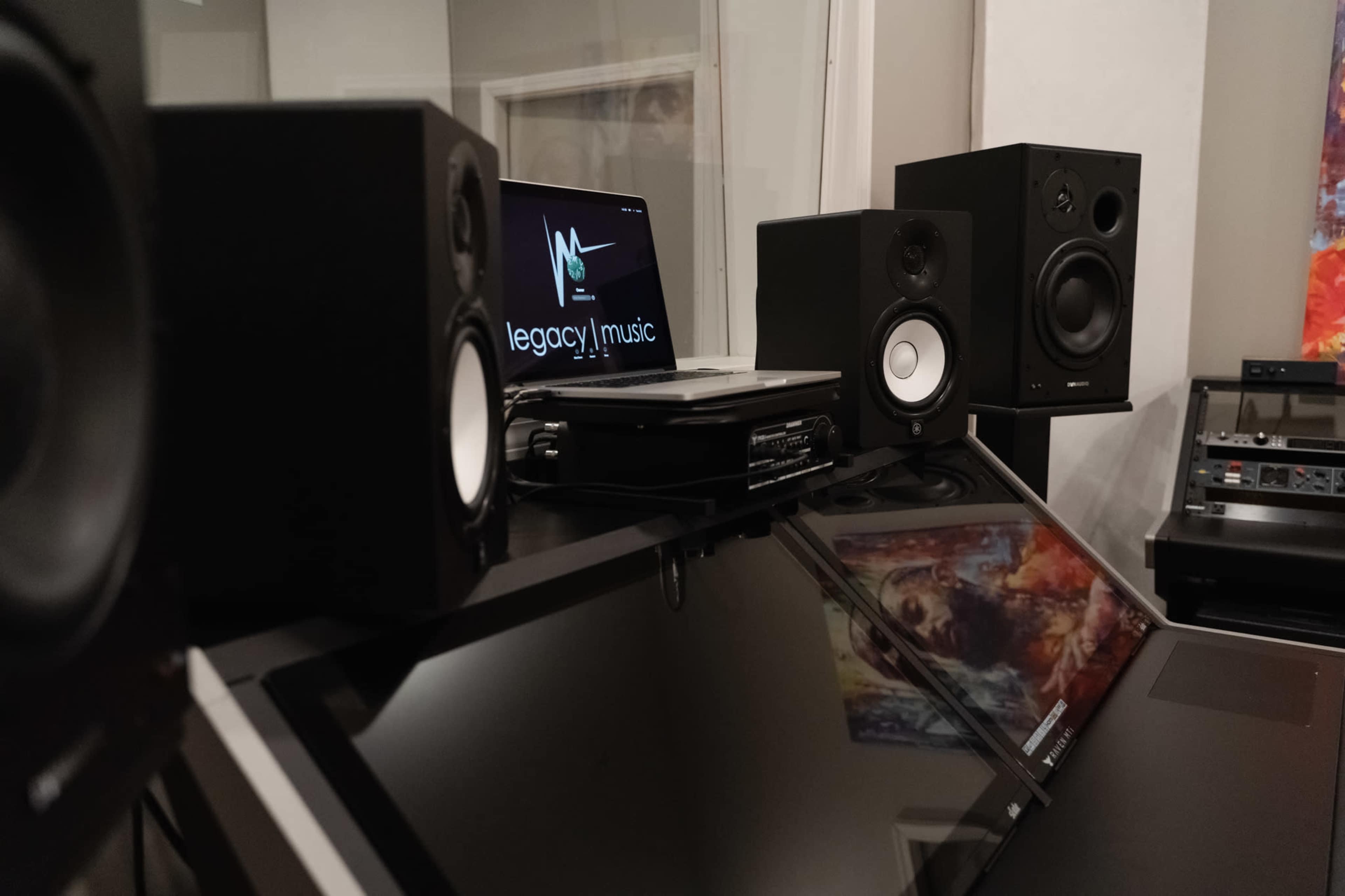 A music production setup featuring speakers, a laptop with a logo, and a sleek surface reflecting the equipment.