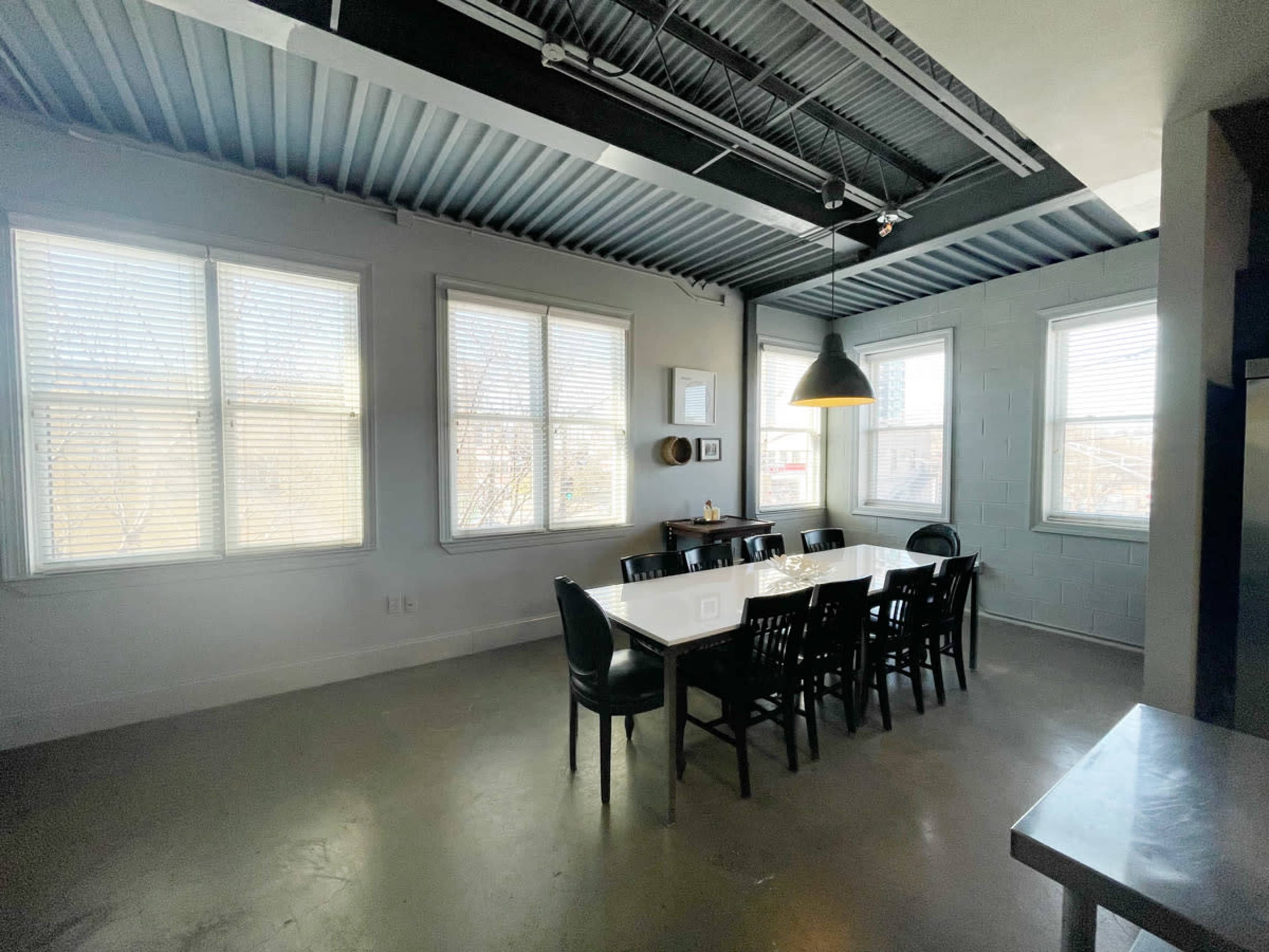 A bright dining area features a long white table surrounded by black chairs and large windows.