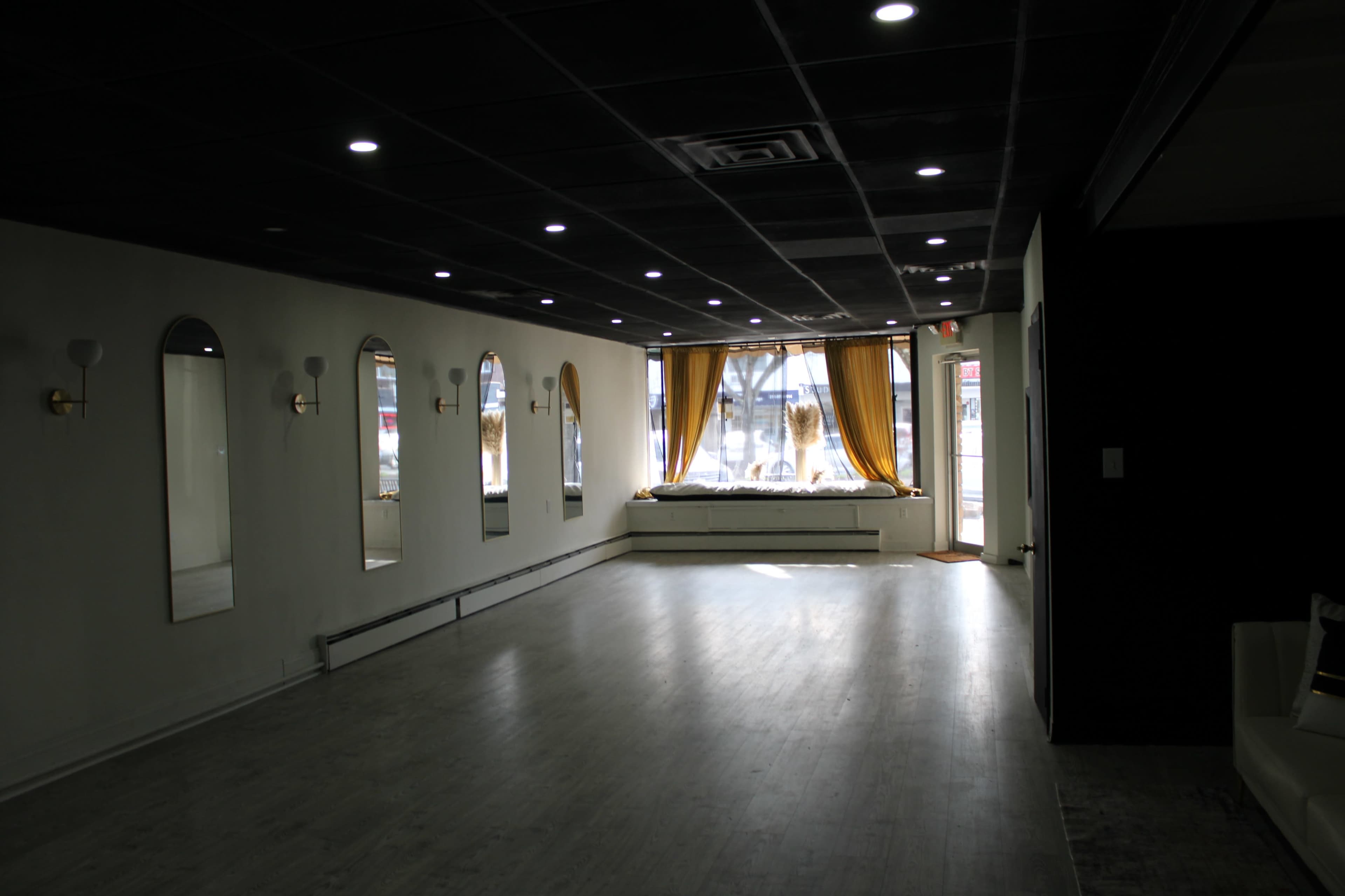 The image shows an empty interior space with large windows, elegant mirrors on the walls, and a decorative curtain by the window.
