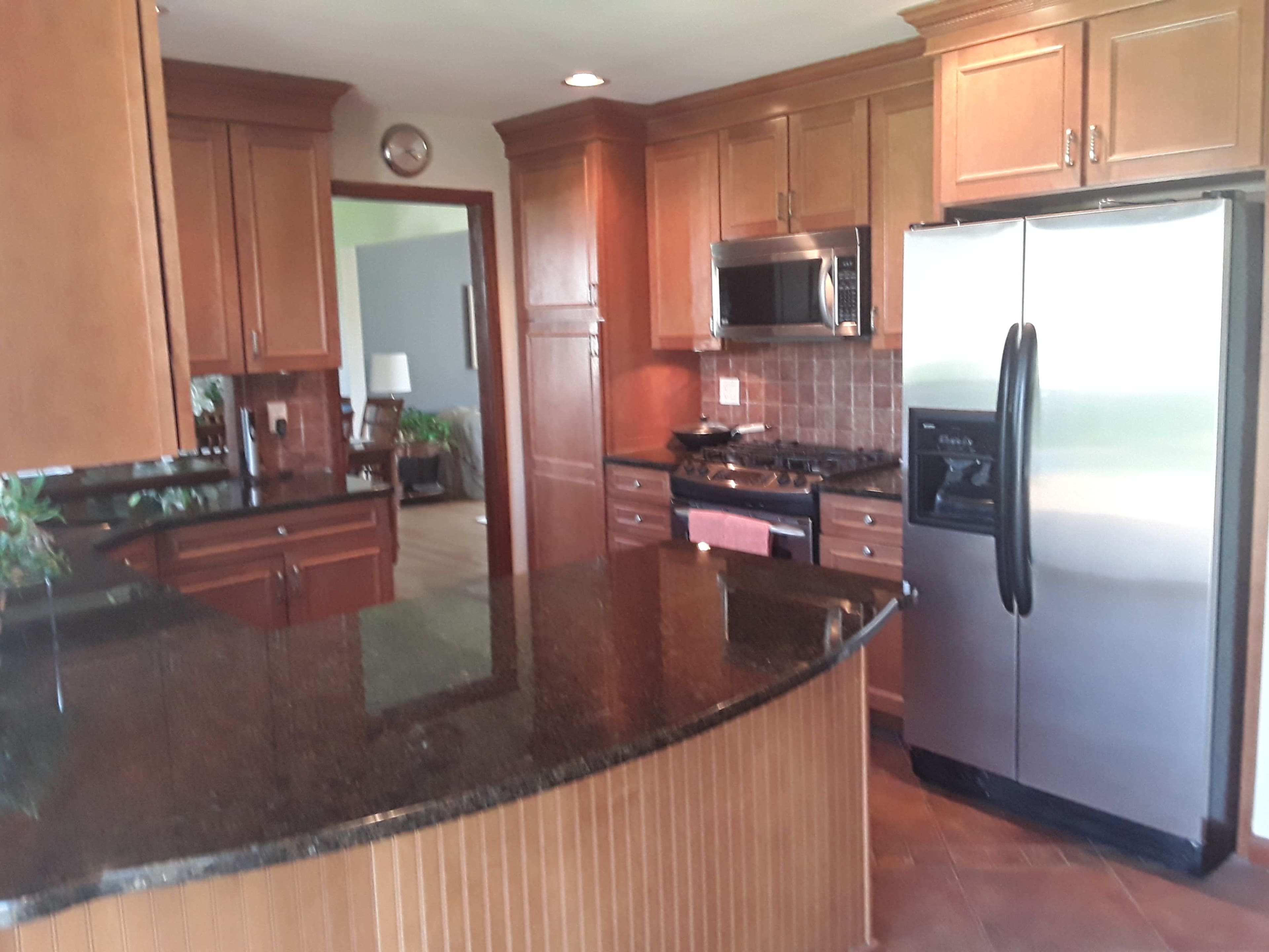 A modern kitchen with wooden cabinetry, a stainless steel refrigerator, and a black granite countertop, featuring a gas range and microwave built into the cabinetry.