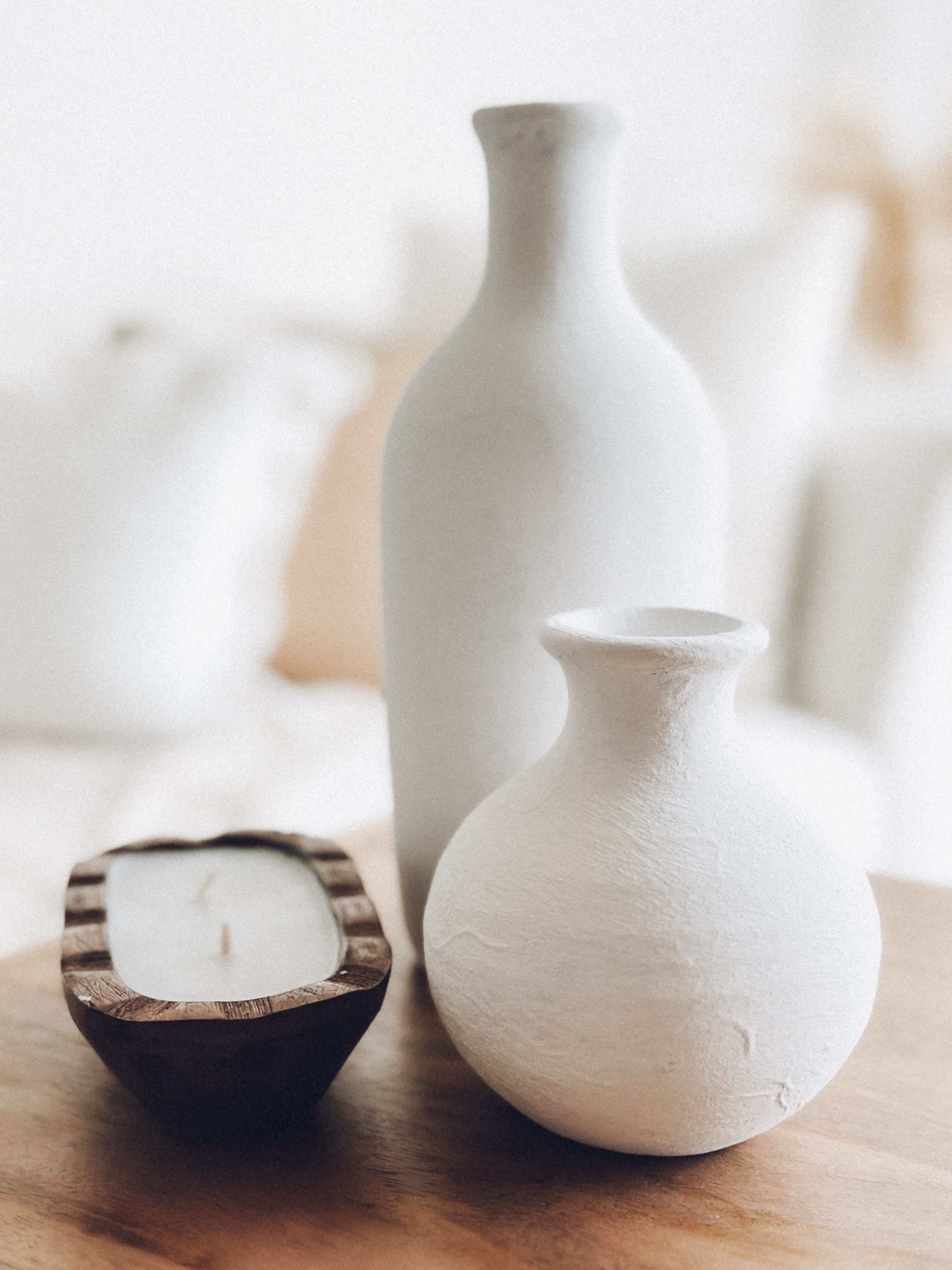 Two white ceramic vases and a wooden tray containing a candle on a wooden surface.