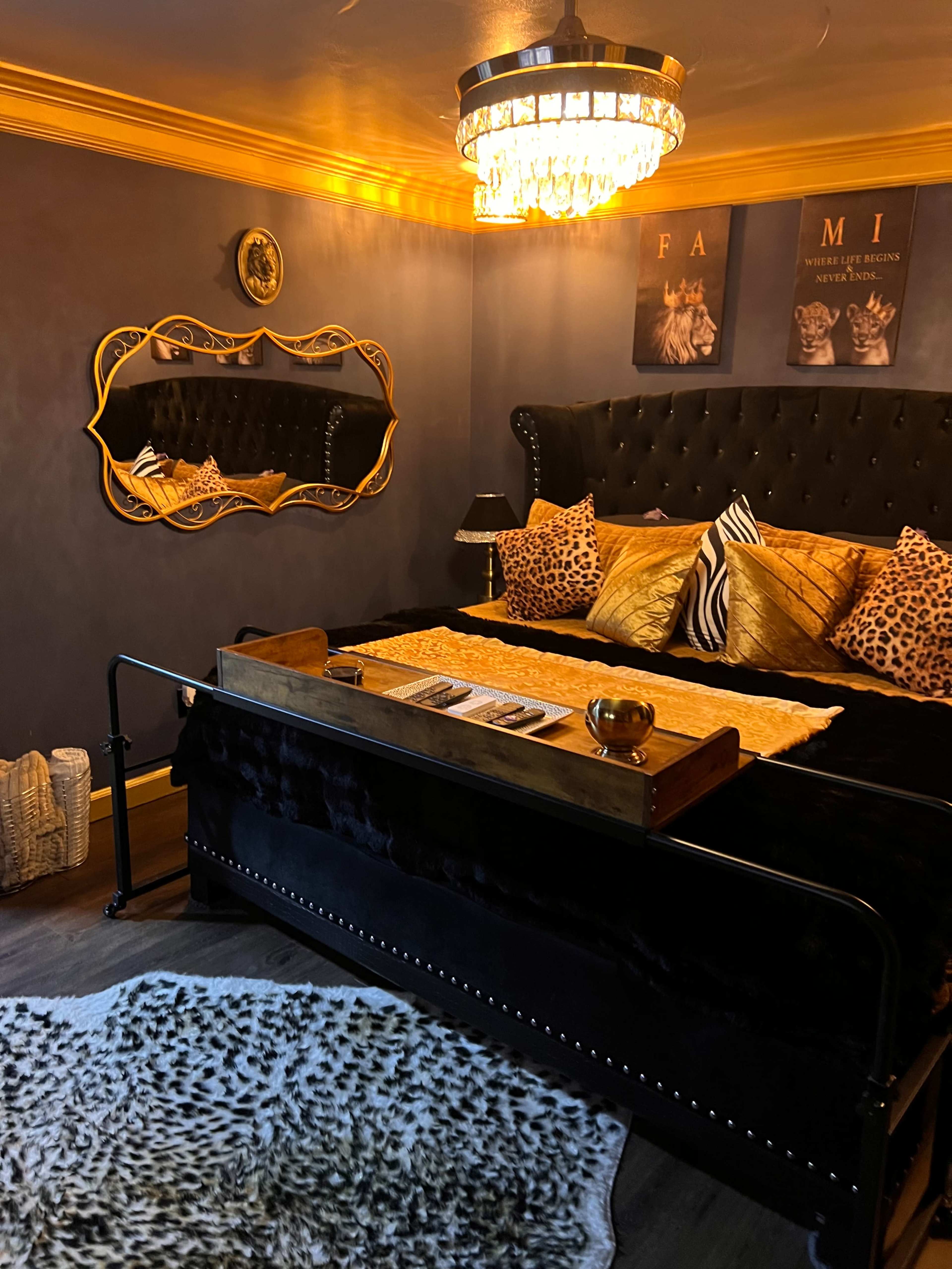The image shows a luxurious bedroom with a black velvet bed, gold accents, and animal print decor, featuring a large chandelier and a decorative mirror on the wall.