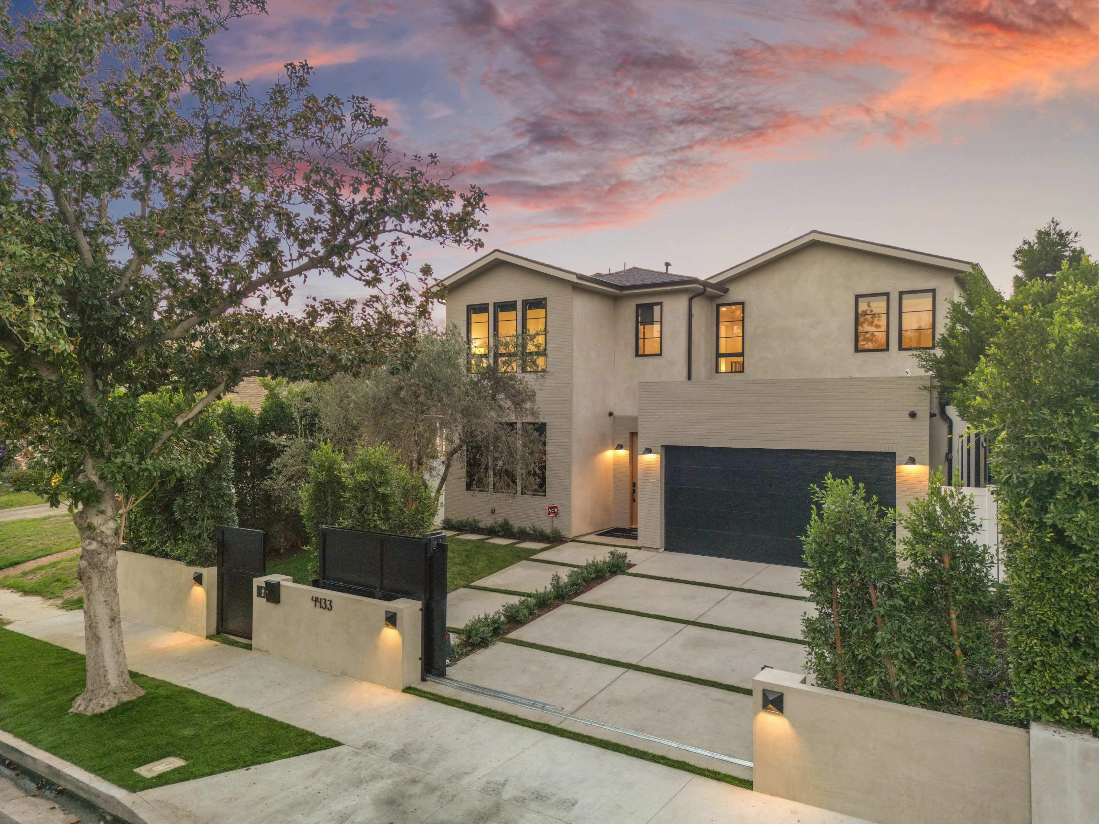 The image shows a modern two-story house with a black garage door and landscaped front yard, situated on a quiet street at dusk.