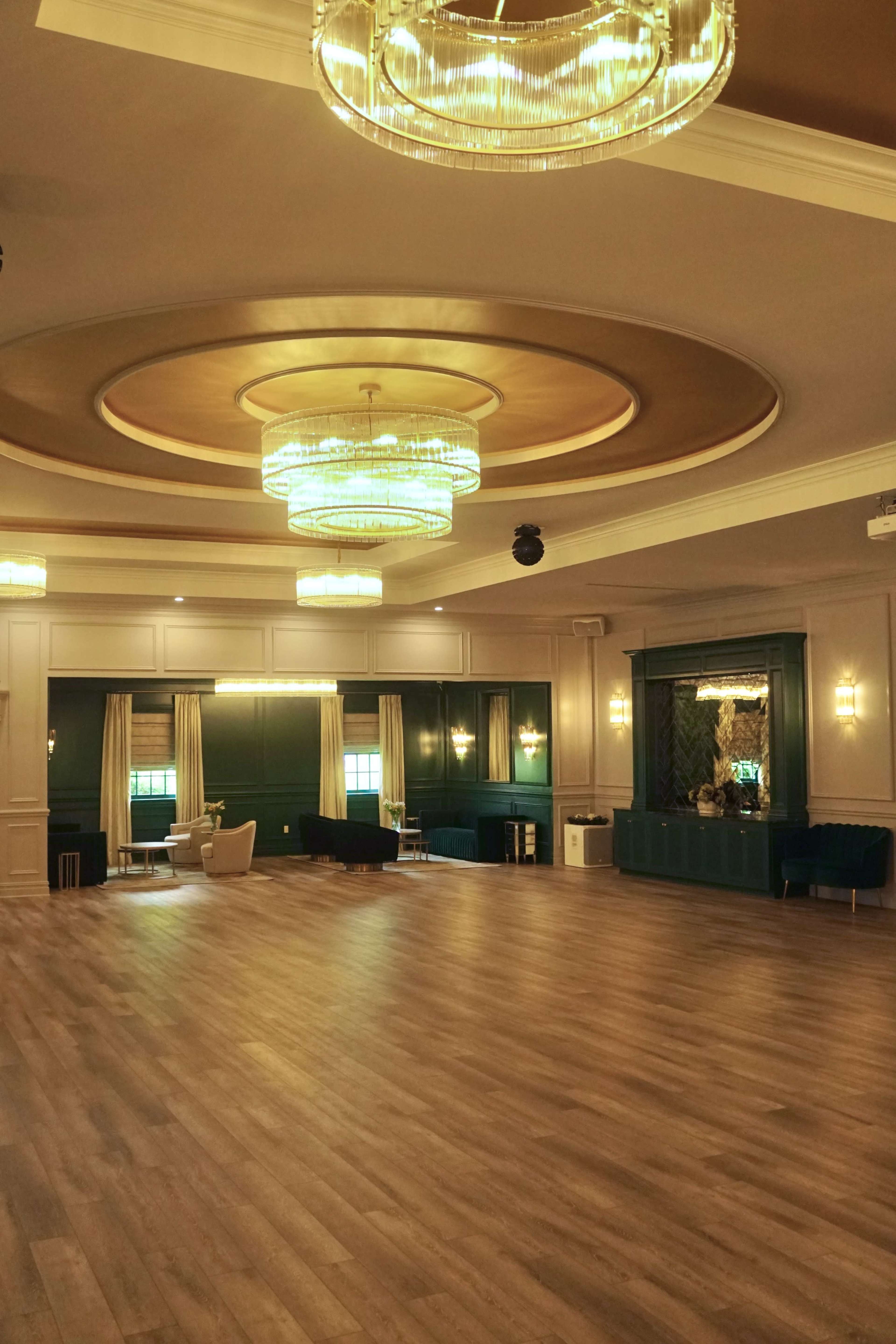 The image shows a spacious interior room with wooden flooring, decorative chandeliers, and elegant furnishings against a teal and gold color scheme.