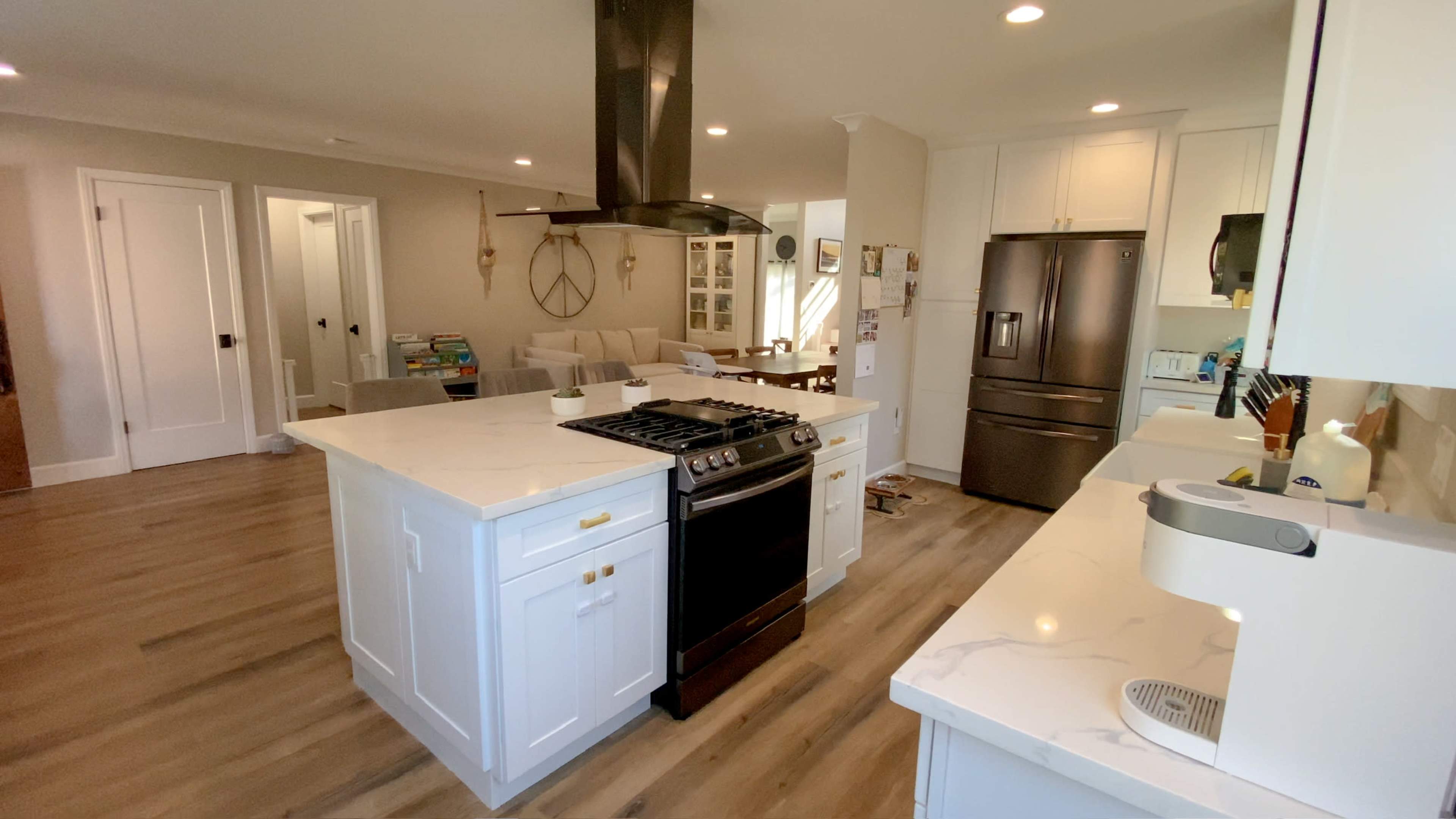 The image shows a modern kitchen featuring a central island with a stovetop, stainless steel appliances, and white cabinetry.