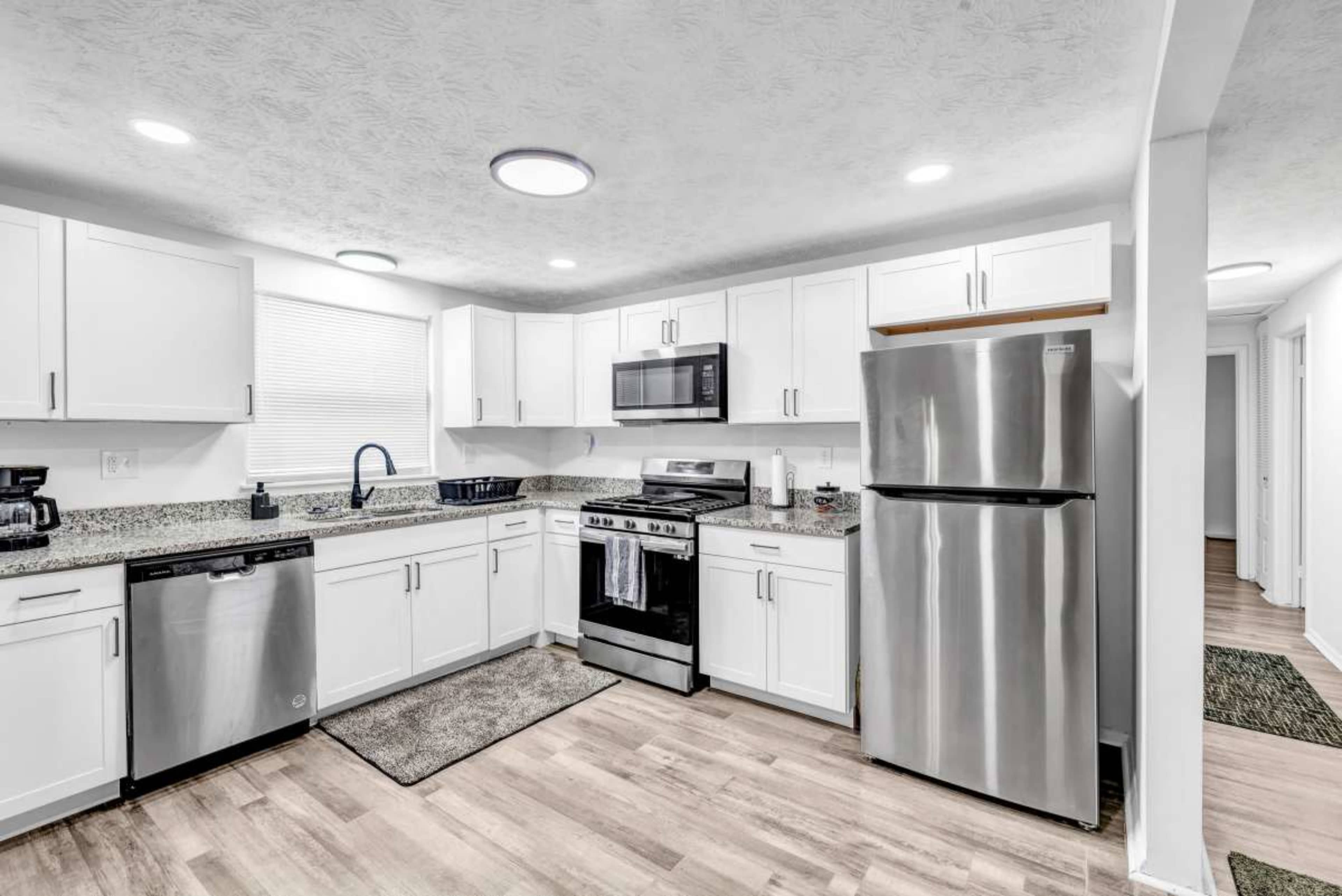 The image shows a modern kitchen with white cabinets, stainless steel appliances, and a granite countertop.
