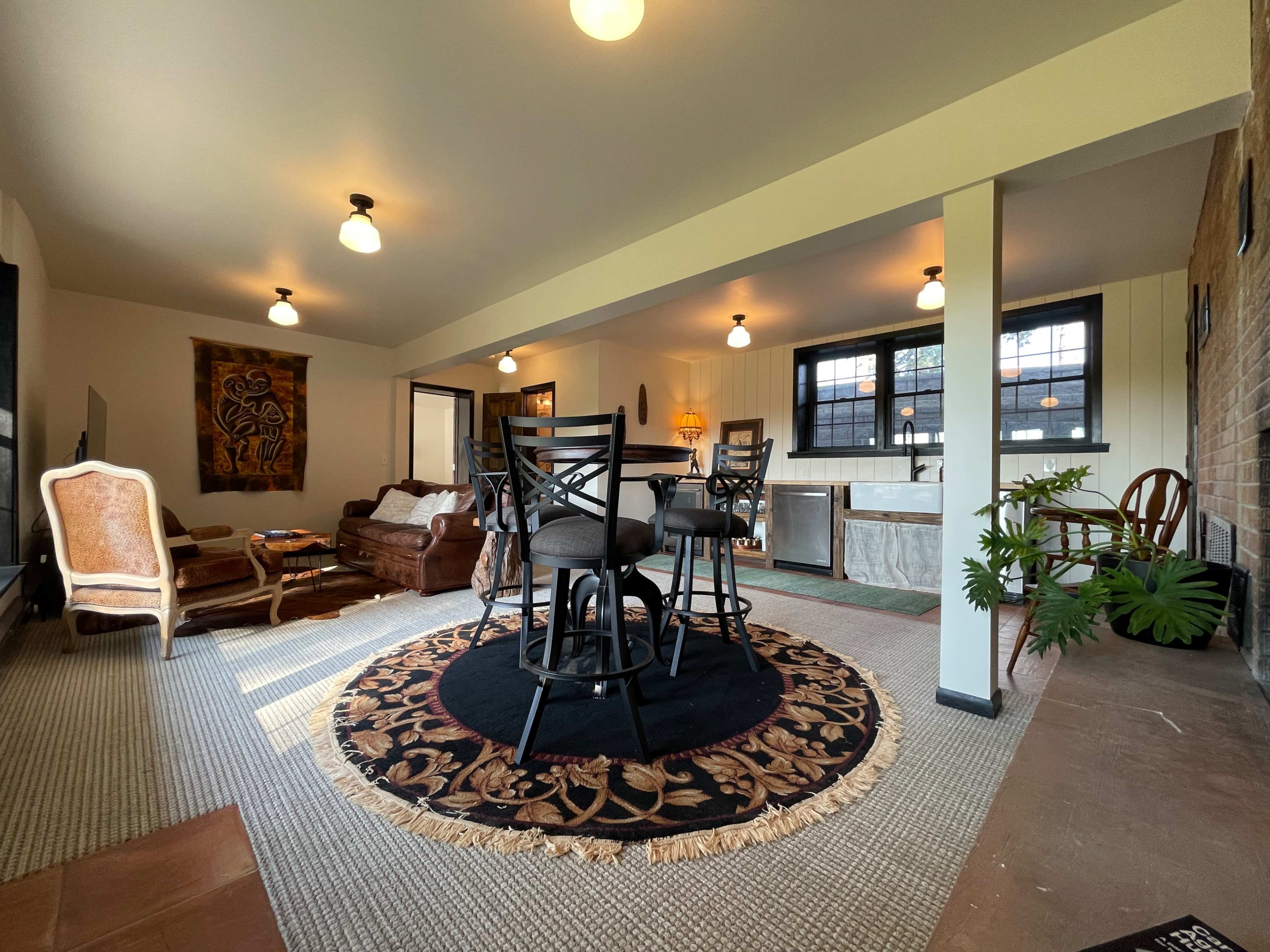 A spacious living area with a dining table and chairs, a brown sofa, and various decorative plants and artwork.