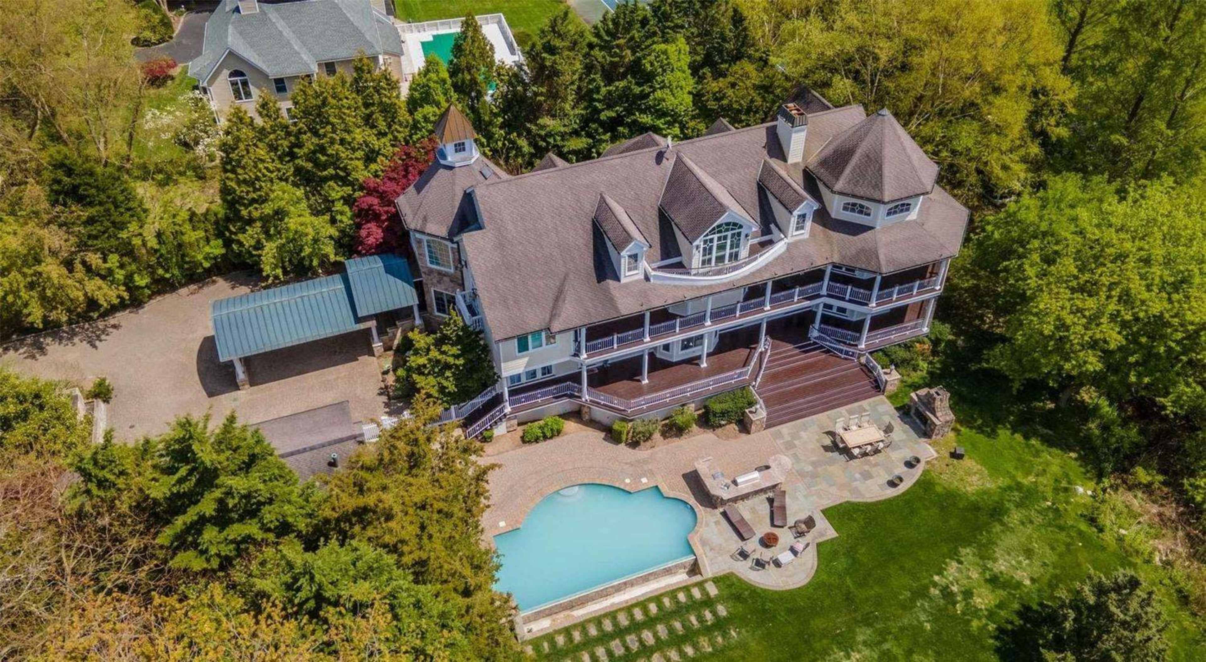 The image shows a large, multi-story house with a distinct architectural style surrounded by trees, featuring a swimming pool and patio area in the backyard.