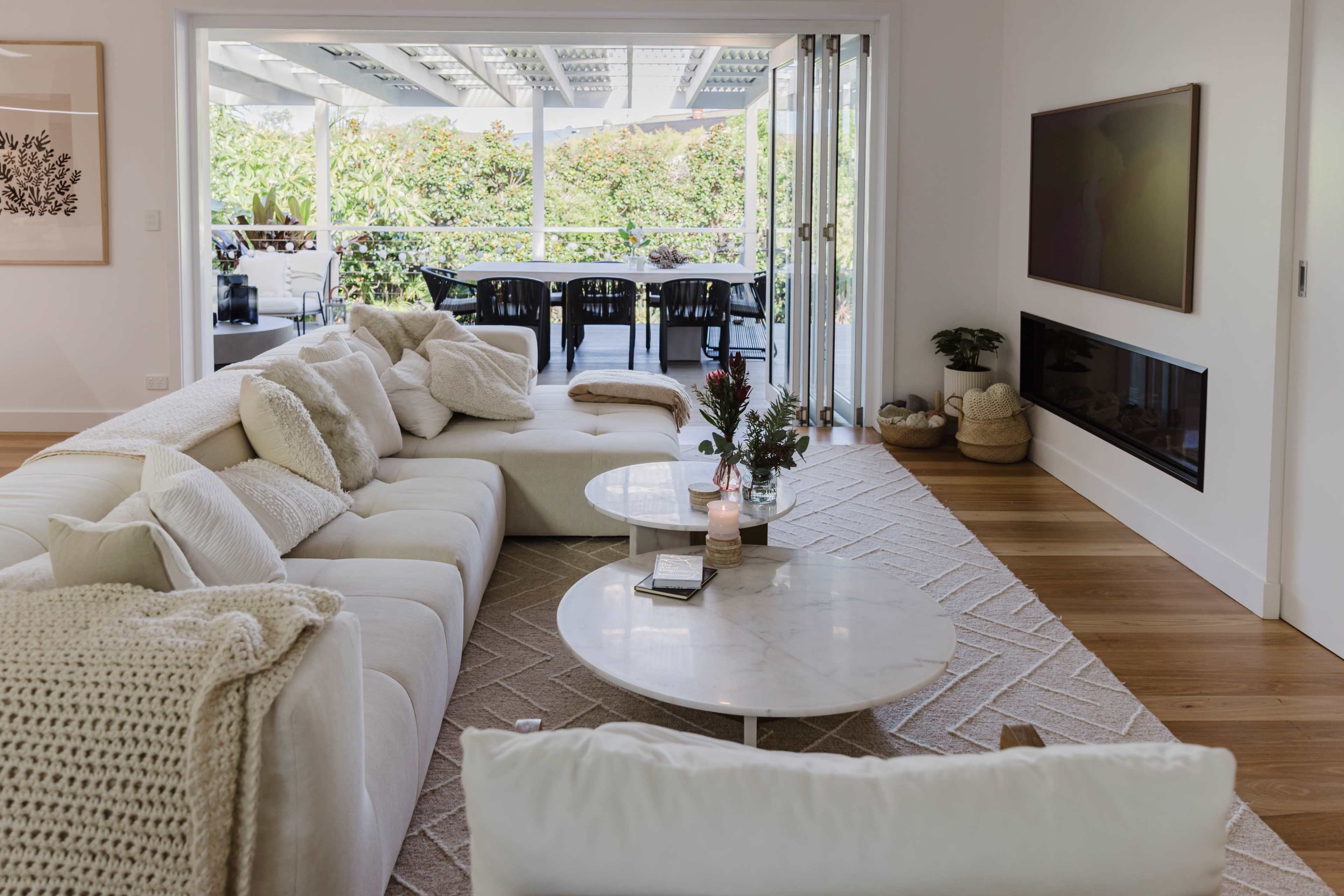 The image shows a modern living room with a large white sectional sofa, two marble coffee tables, and a view of a patio through sliding glass doors.
