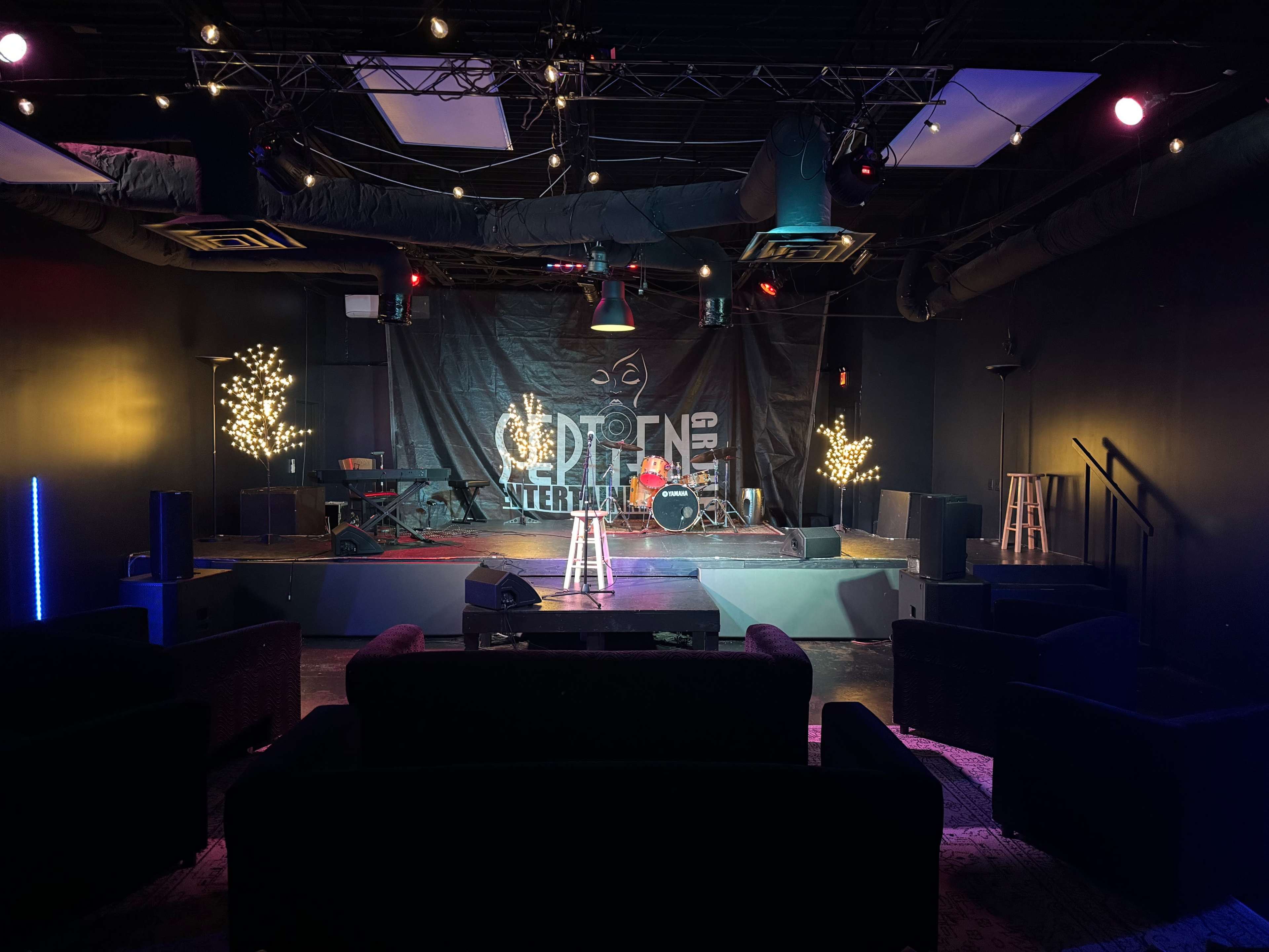 A performance stage in a dimly lit venue, featuring musical instruments, seating areas, and decorative lights.
