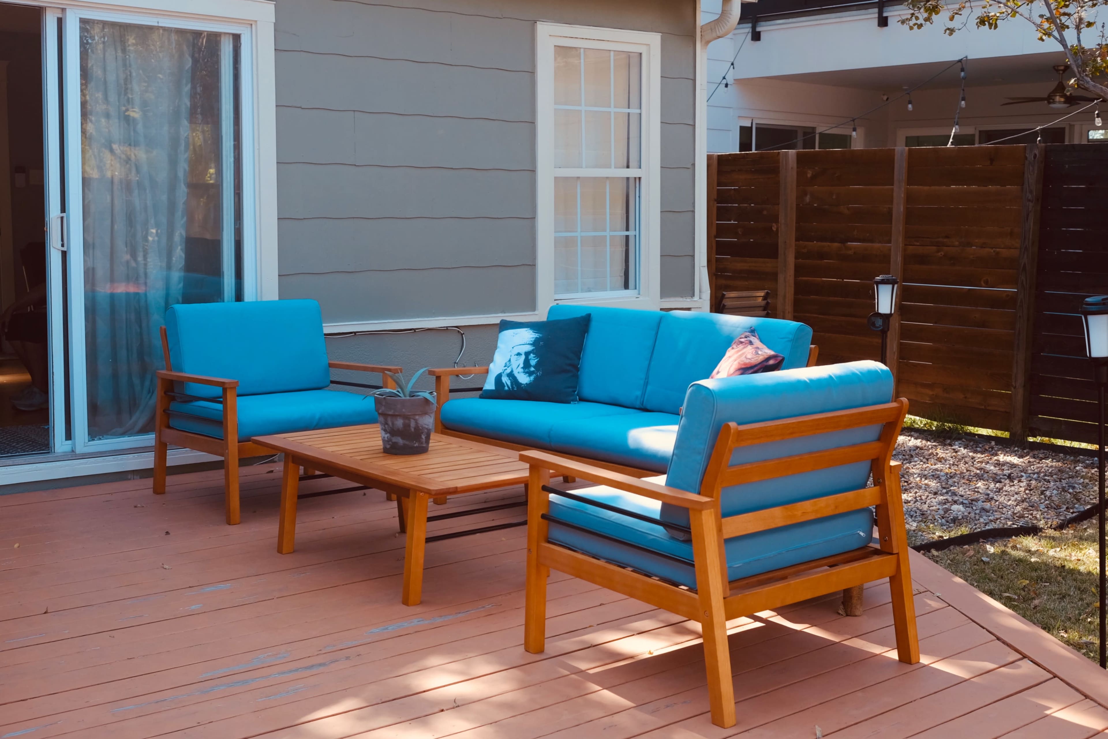 The image shows a patio area with a blue sofa and two matching chairs arranged around a wooden coffee table.