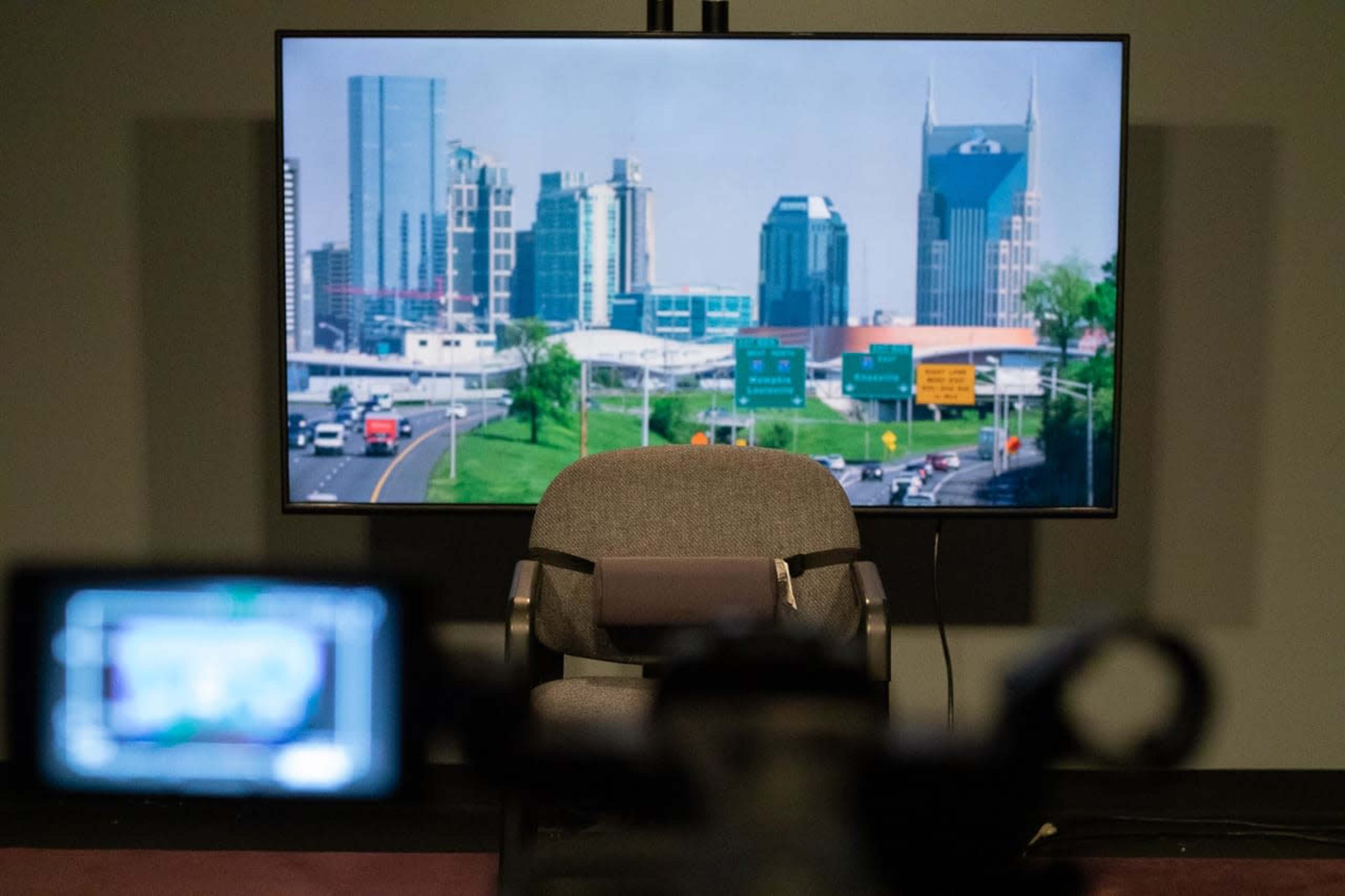 A studio setup features an empty chair in front of a screen displaying a city skyline with highway signs.