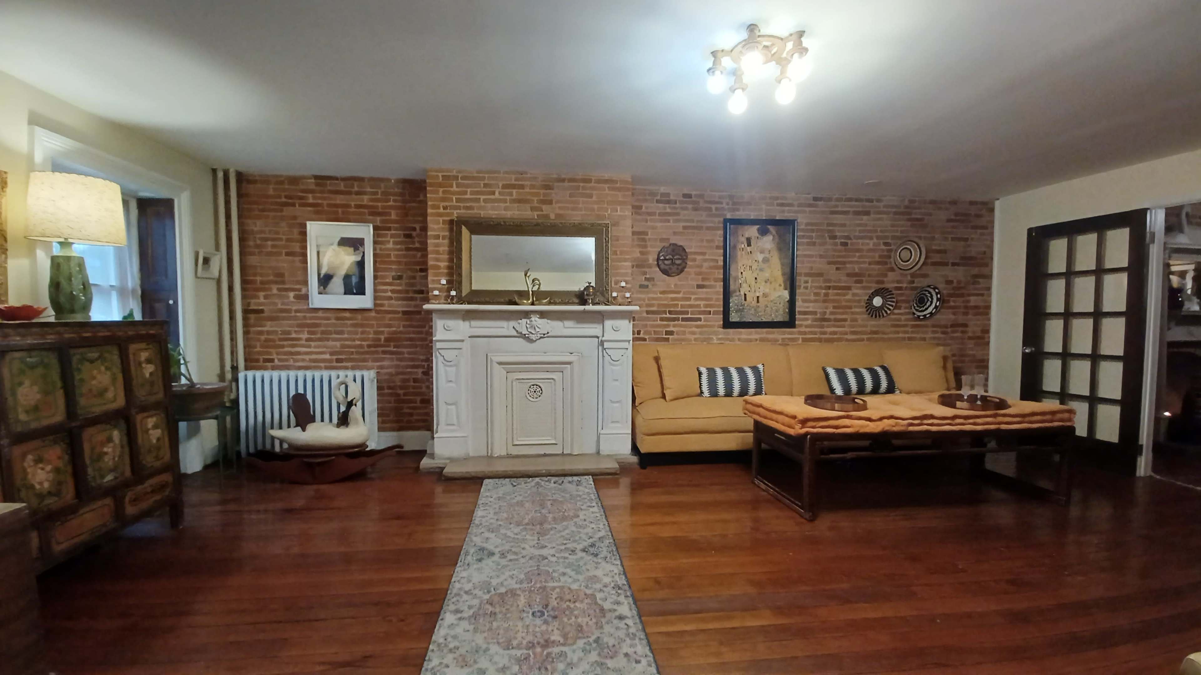 The living room features a brick wall, a white mantelpiece, a yellow sofa, and a wooden coffee table on a patterned rug.