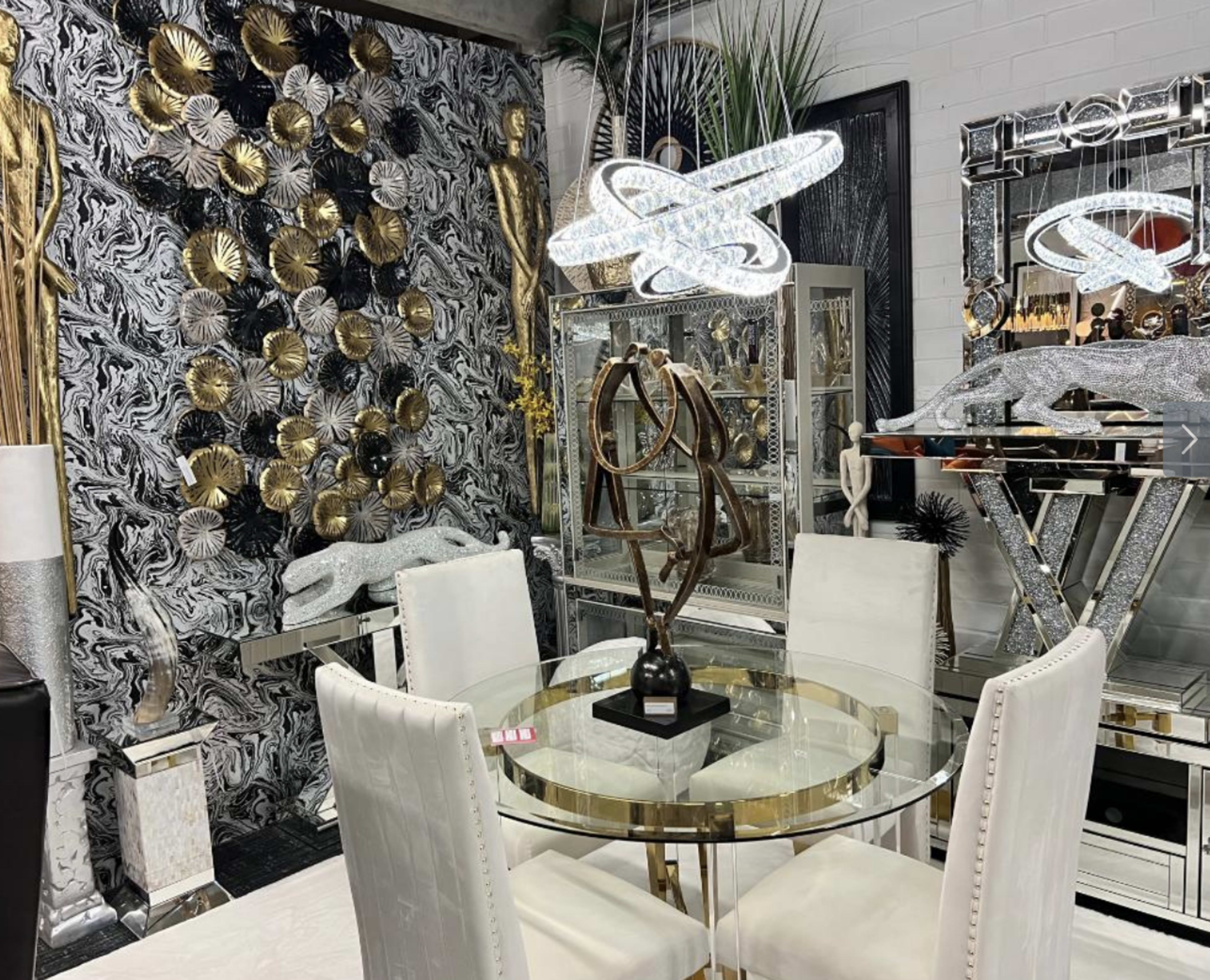 A modern dining area with a glass table surrounded by white upholstered chairs, set against a striking wall adorned with decorative gold and black elements.
