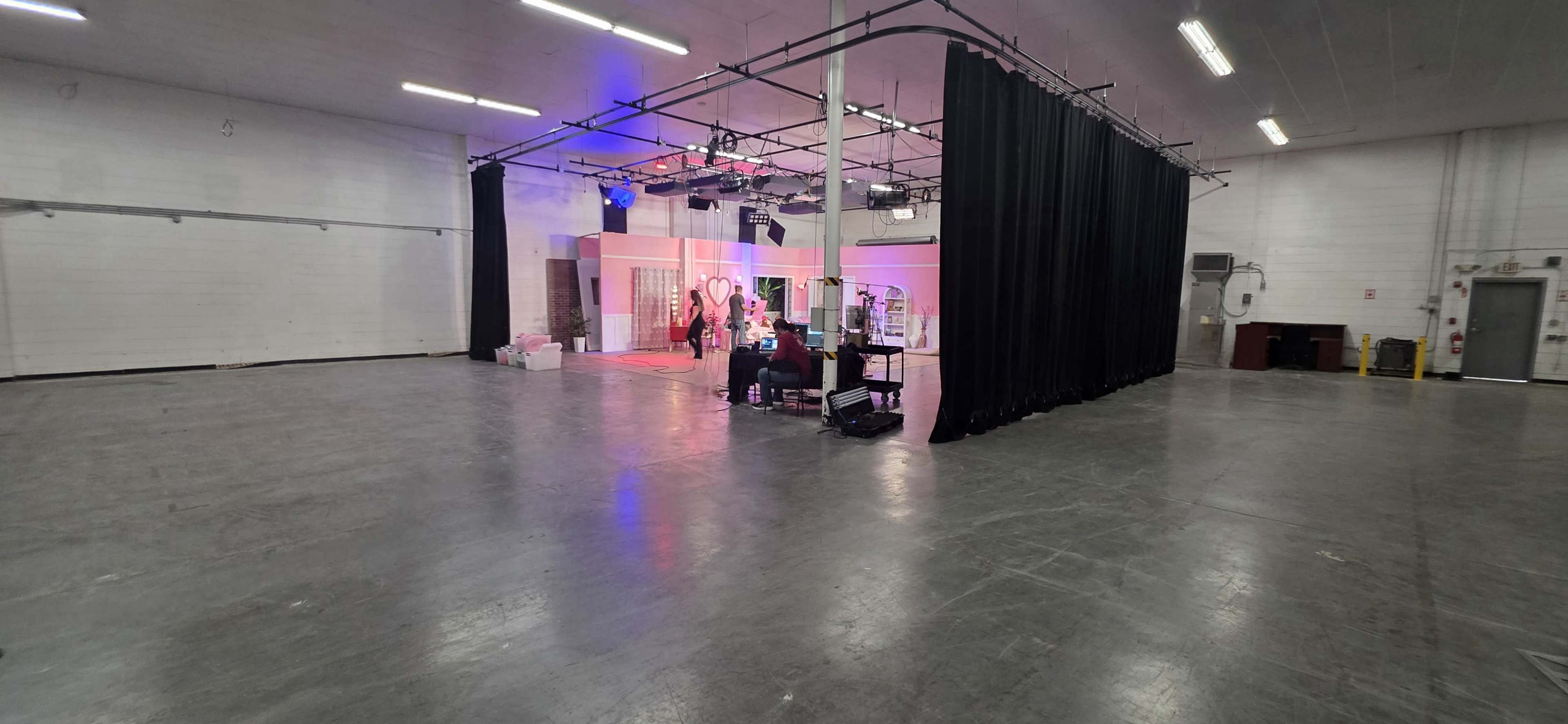 The image shows an empty industrial space with a sectioned-off area featuring stage lights, a backdrop, and equipment.