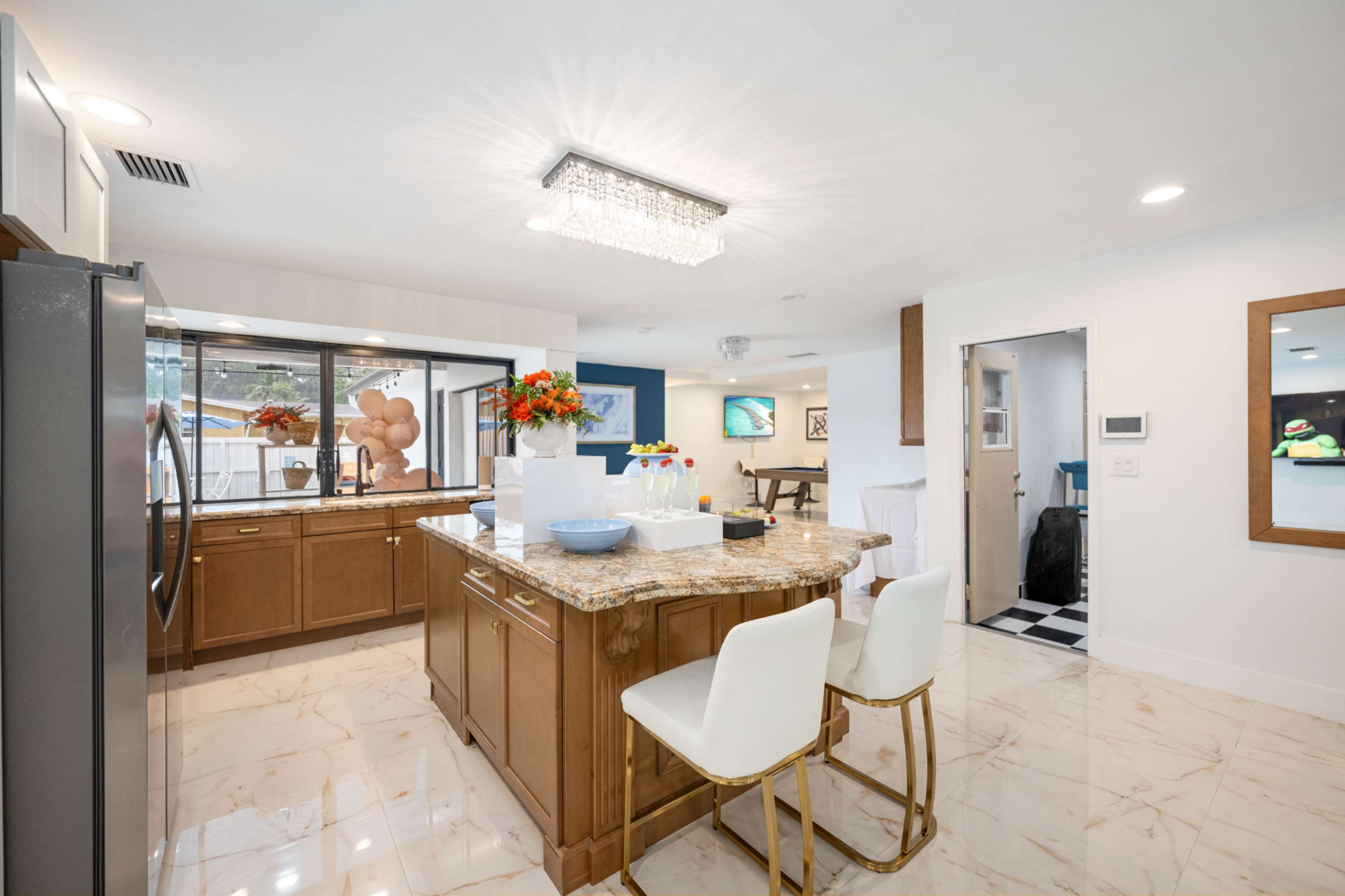 The image shows a modern kitchen featuring a central island with a granite countertop, stainless steel appliances, and a large window that provides natural light.