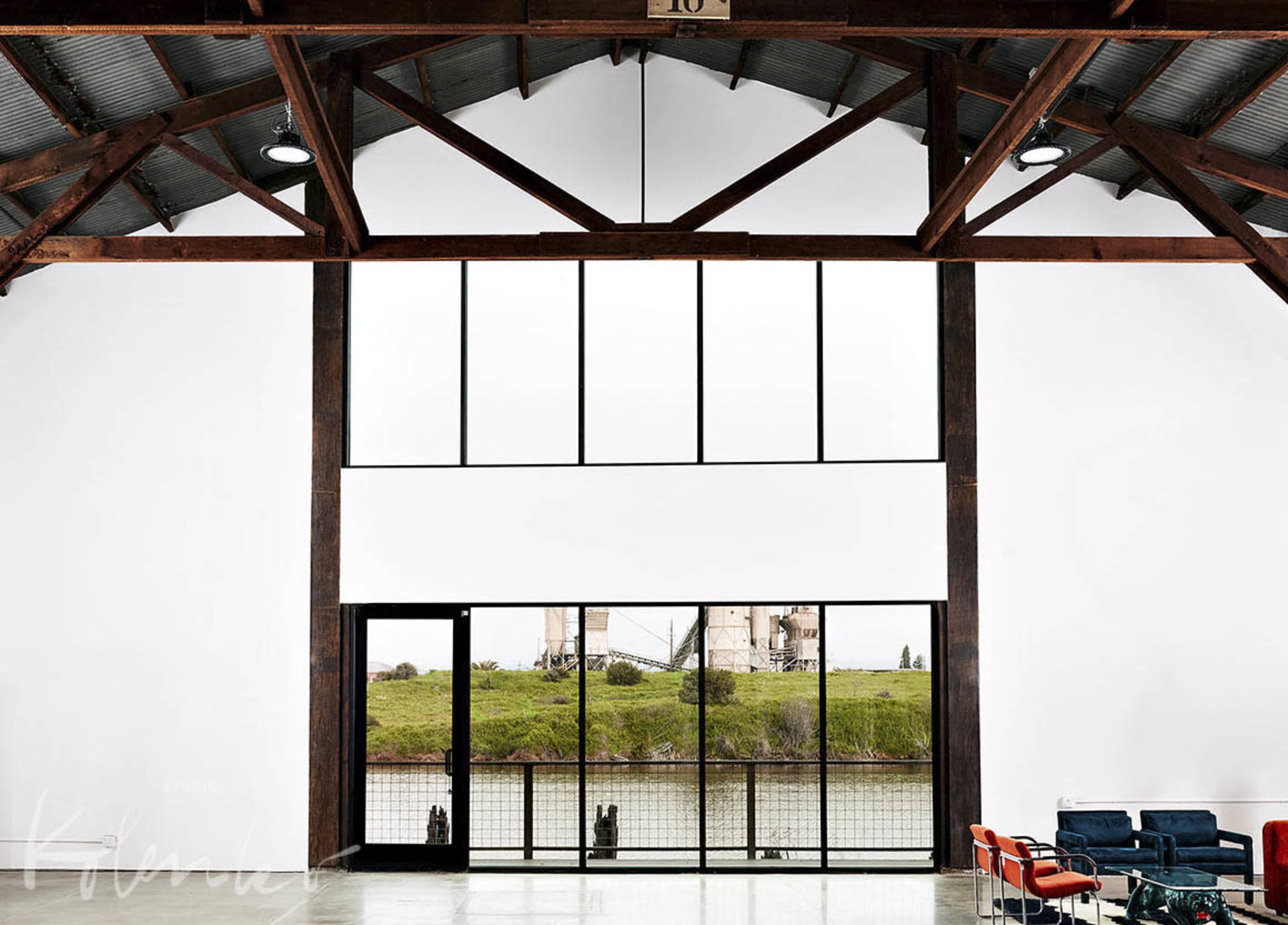 An interior space with large windows overlooking a body of water, featuring wooden beams and modern seating arrangements.
